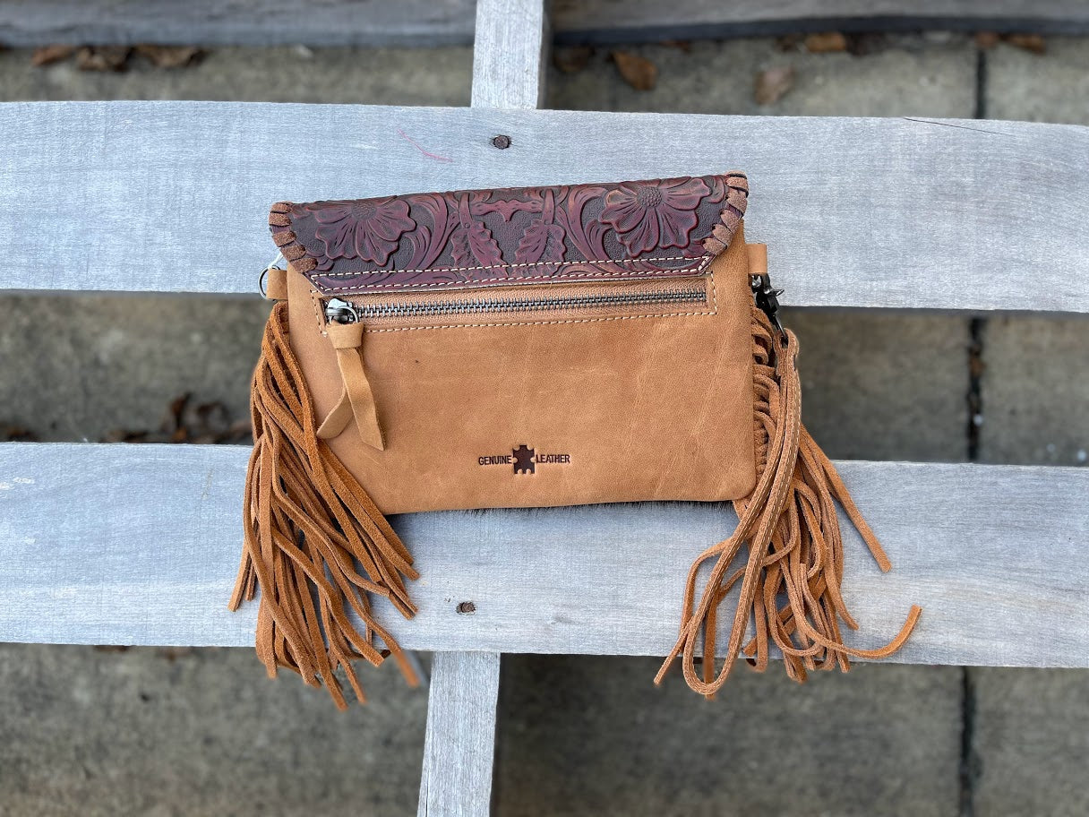 Brown leather handbag with fringe on a wooden surface