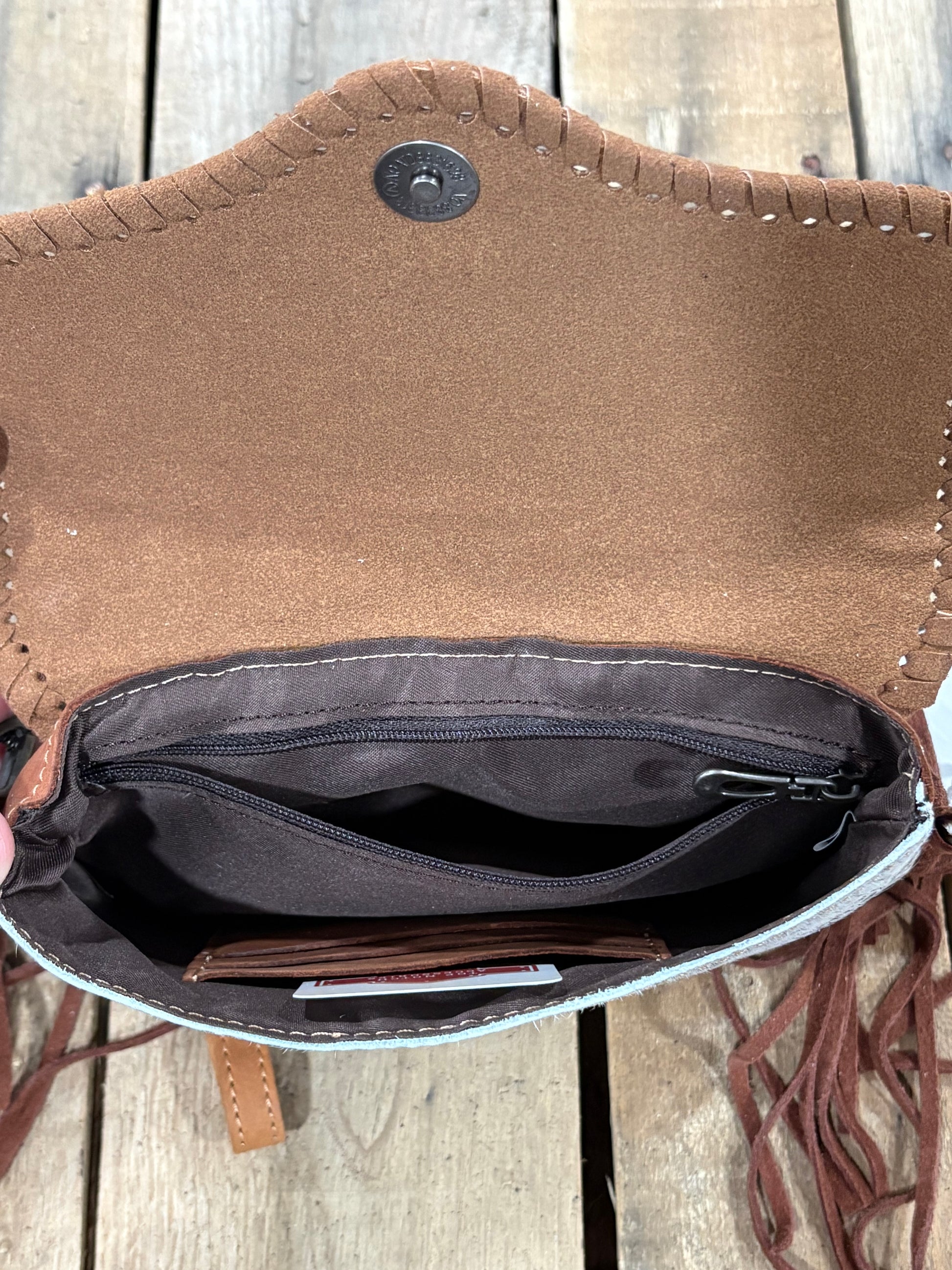 Inside Zipper view of Brown leather crossbody with fringe on a wooden surface