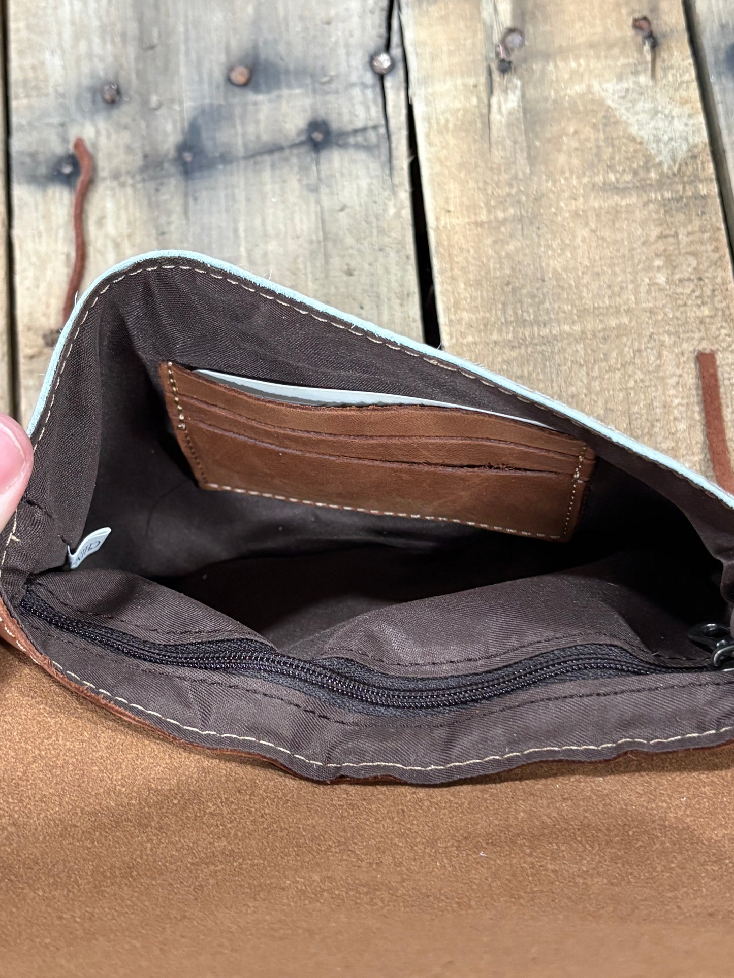 Card slot view of a brown leather crossbody purse on a wooden background