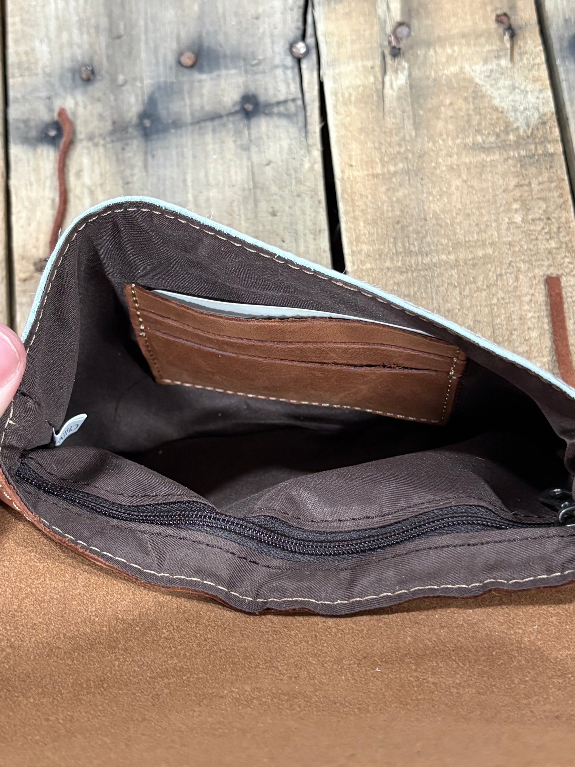 Card slot view of a brown leather crossbody purse on a wooden background