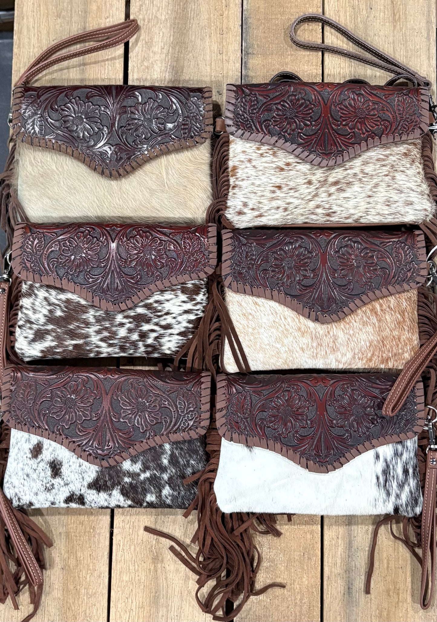 Six crossbody leather handbags with cowhide patterns on a wooden surface