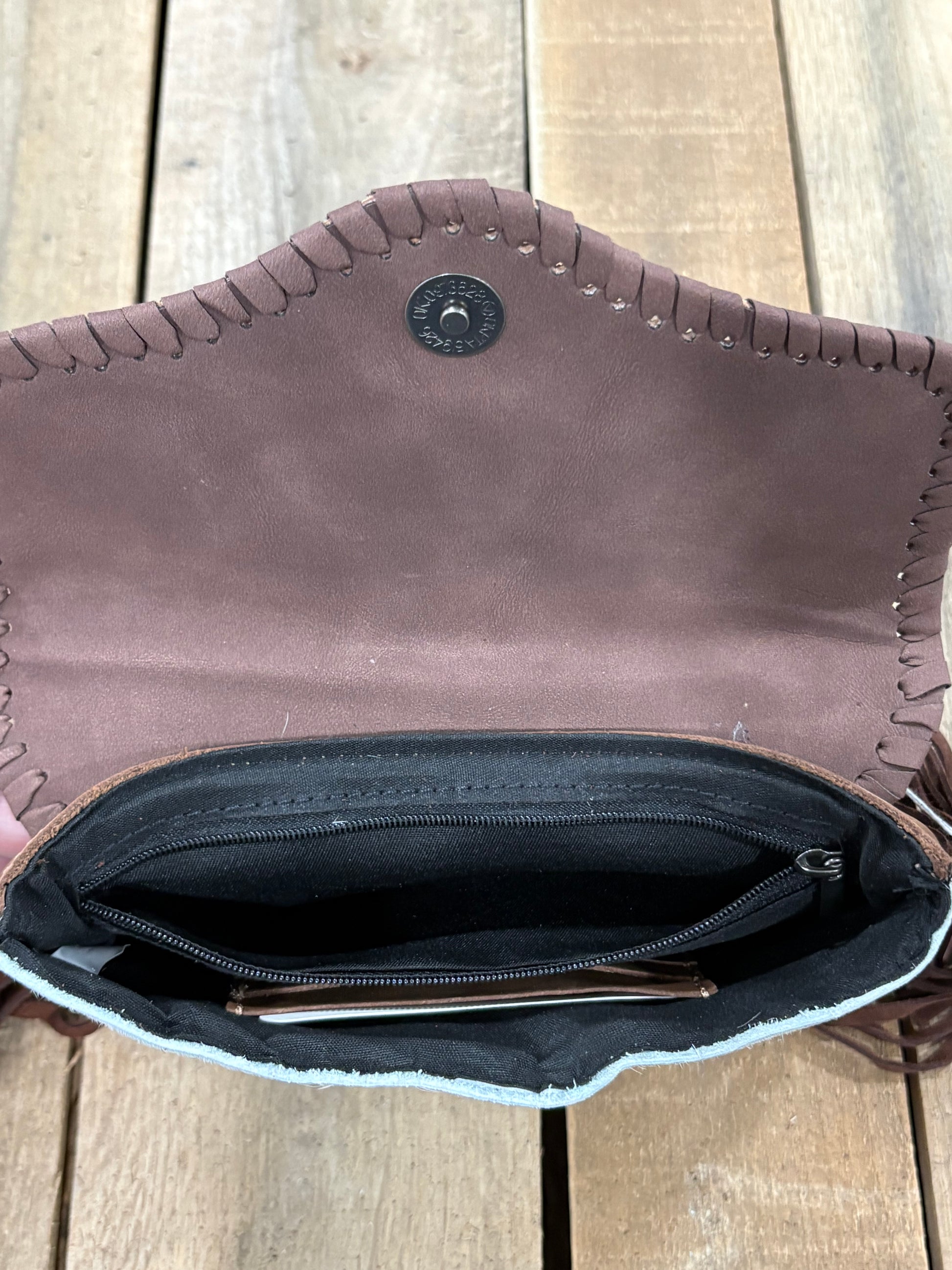 Inside Zipper view of Coffee Brown leather crossbody with fringe on a wooden surface