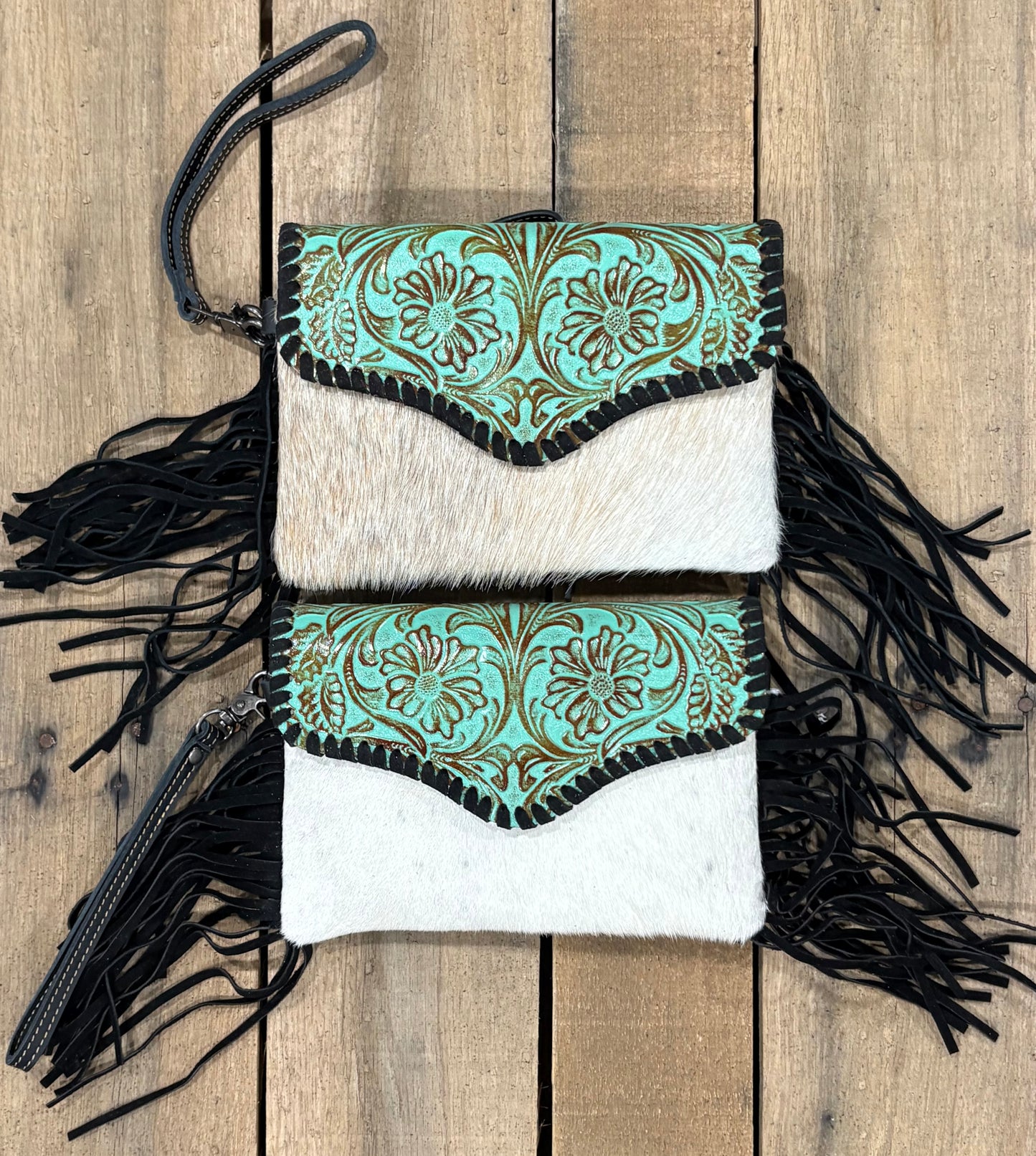 Two cowhide hairon handbags with turquoise pattern and black fringes on a wooden surface