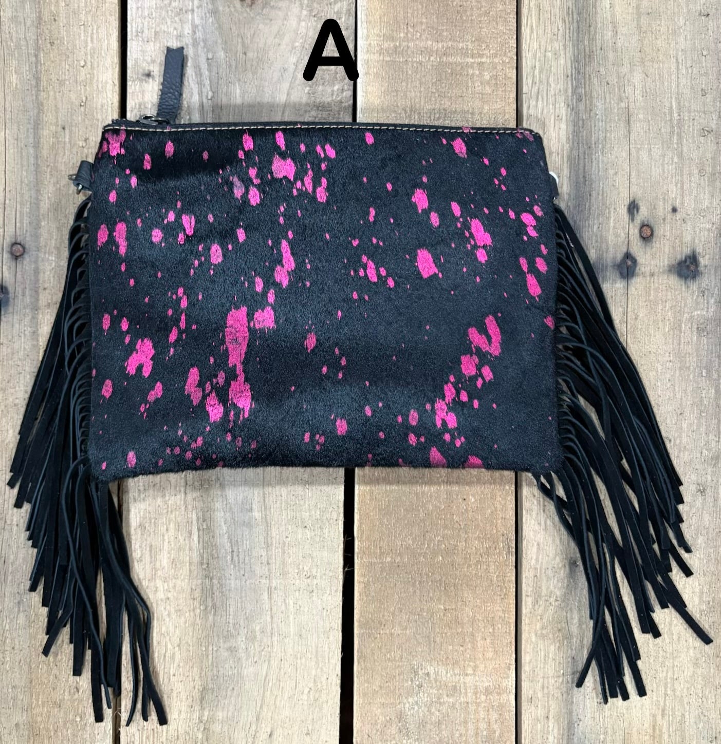 Black clutch with pink speckles and black hairon fringe on a wooden surface