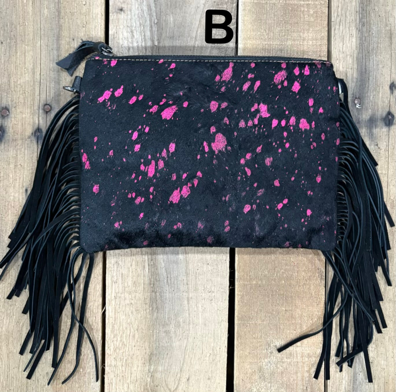 Black clutch with pink speckles and black hairon fringe on a wooden surface
