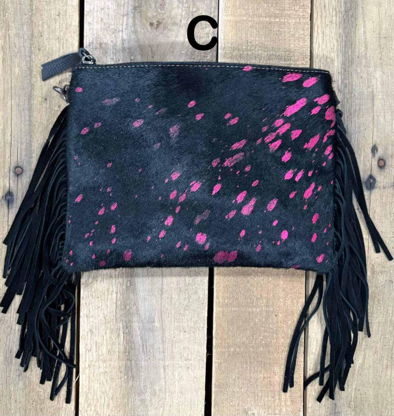 Black clutch with pink speckles and black hairon fringe on a wooden surface