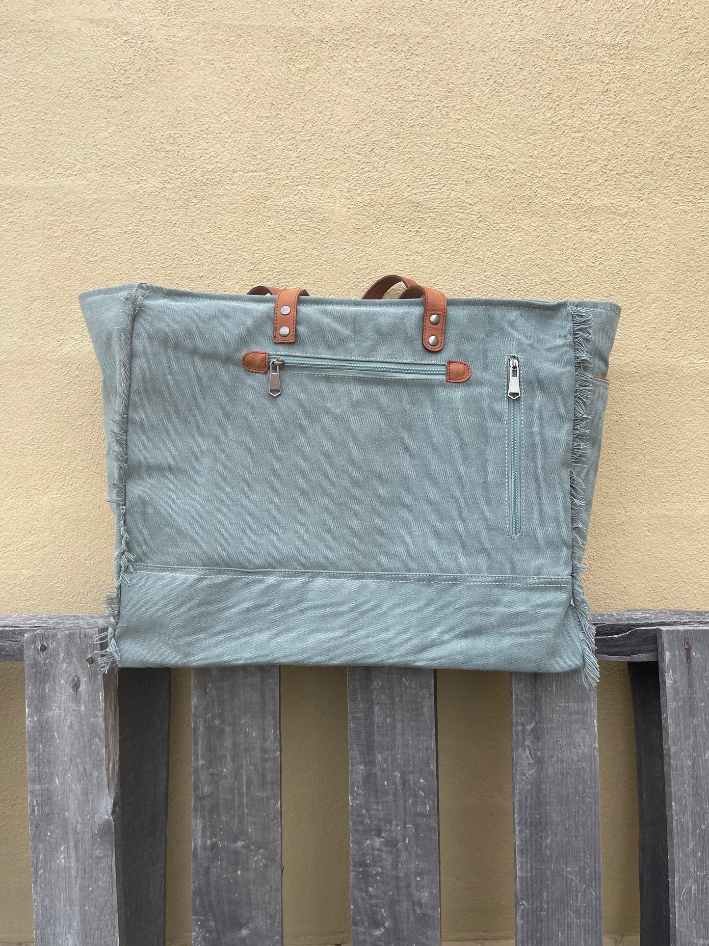 A blue multi canvas and leather conceal carry weekender bag with a geometric pattern. Rear view showing zippered closed pocket and concealed carry pocket. 