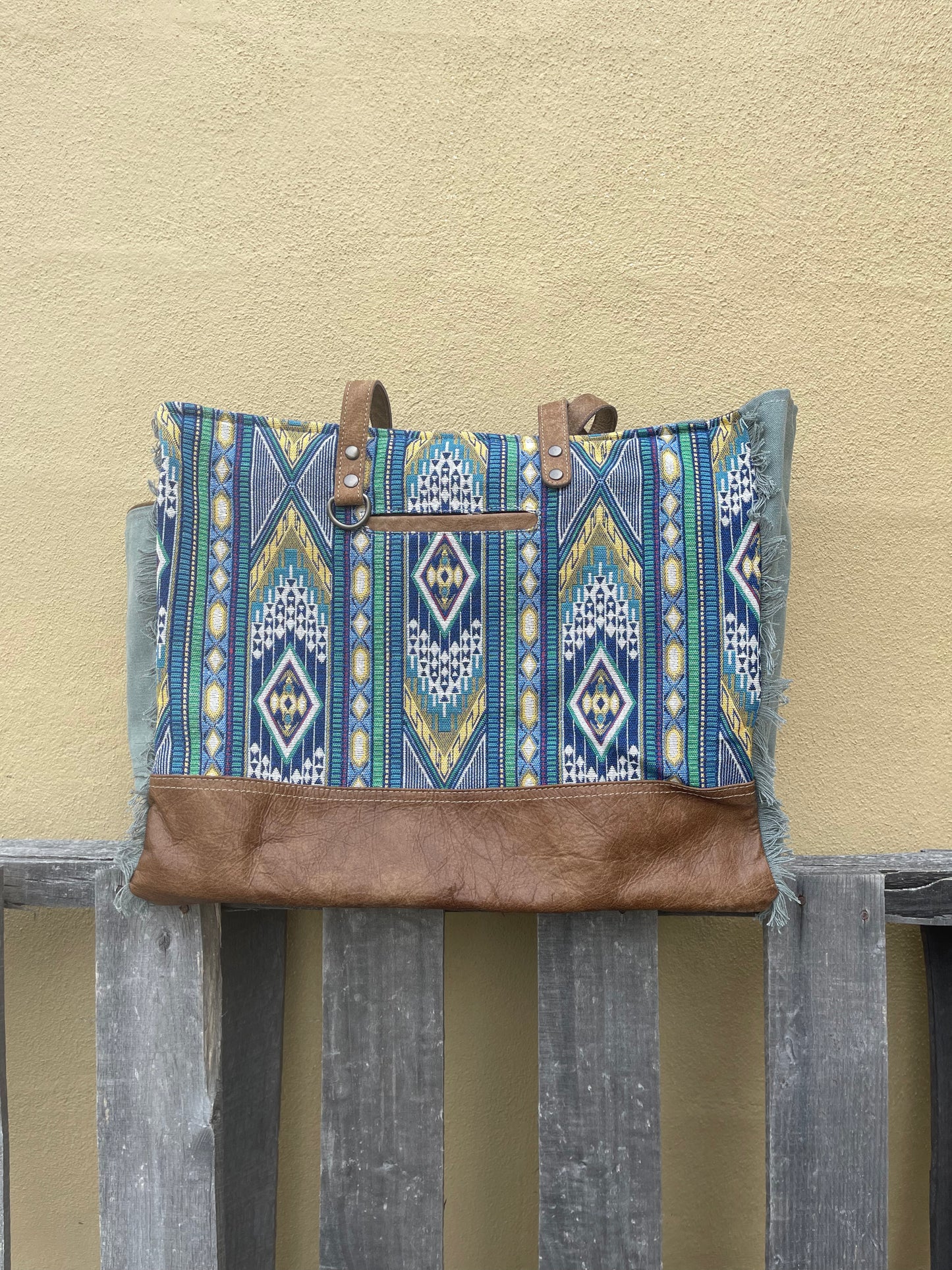 A blue multi canvas and leather conceal carry weekender bag with a geometric pattern. Front view showing front pocket, key ring holder, and shoulder straps. 