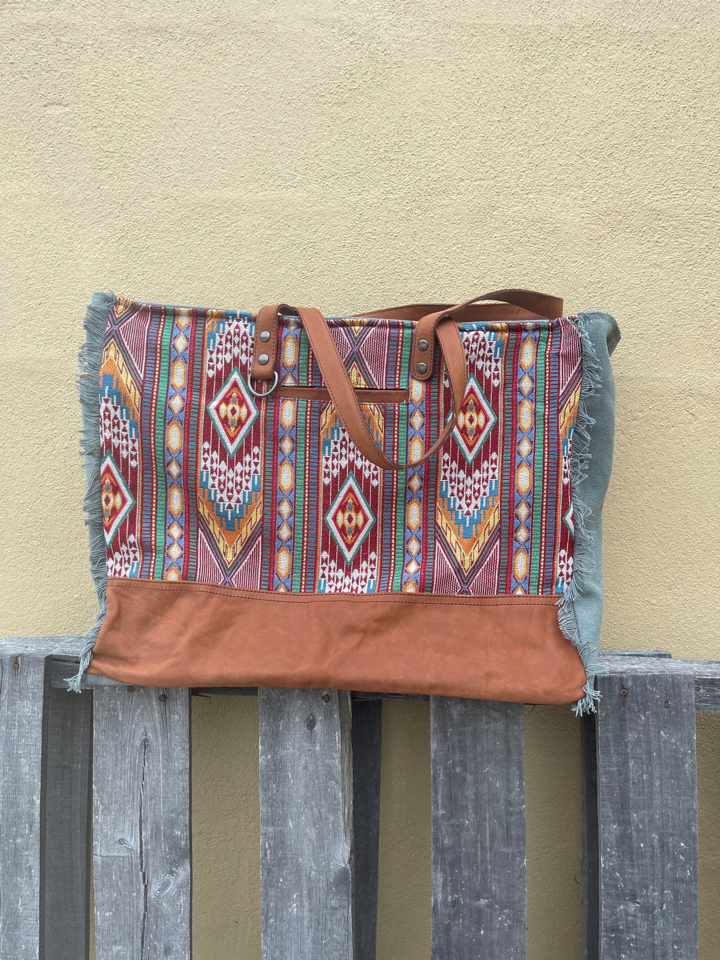 A red multi canvas and leather weekender bag with geometric patterns.  Close up front view. 
