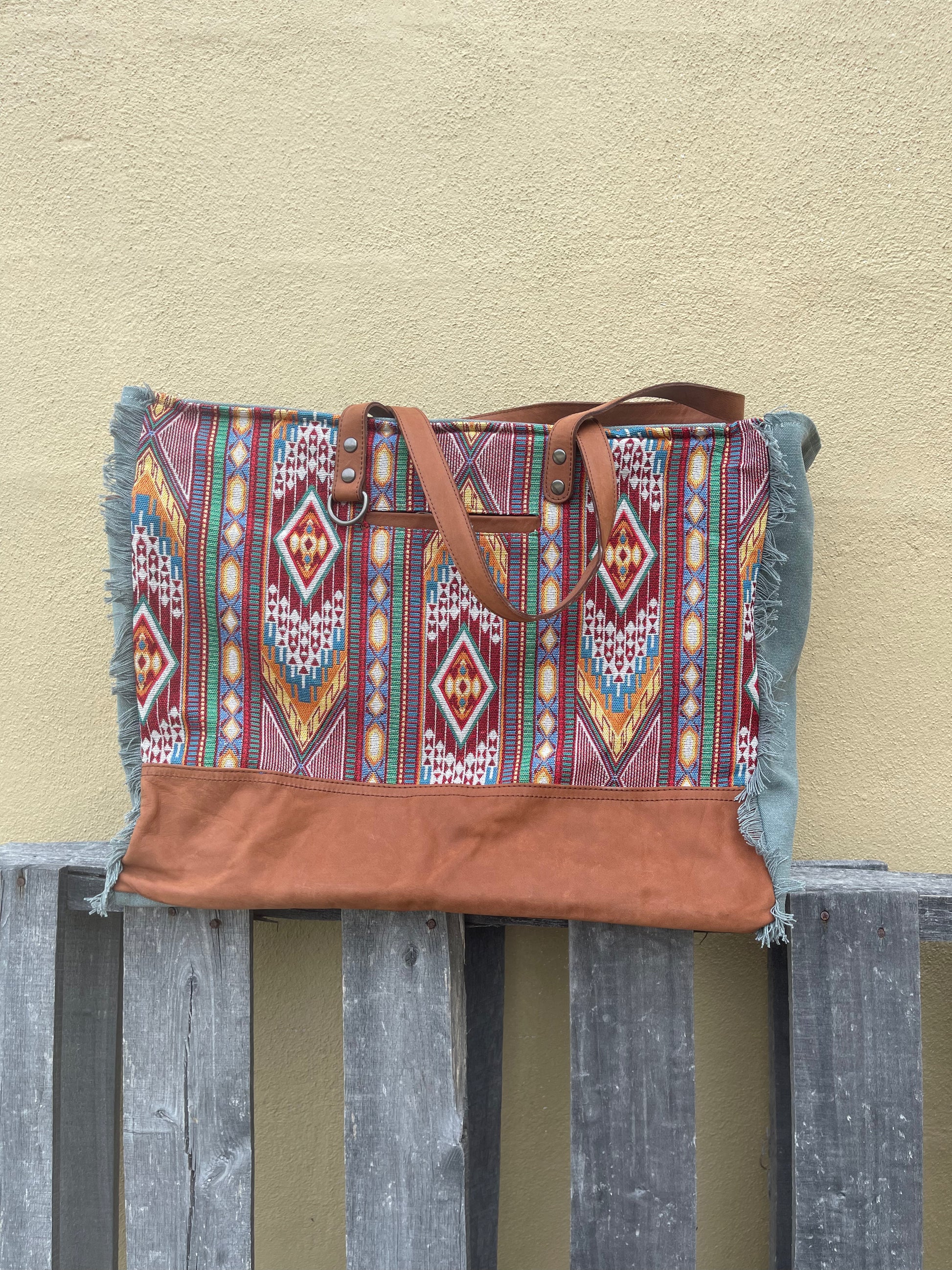 A red multi canvas and leather weekender bag with geometric patterns.  Close up front view. 
