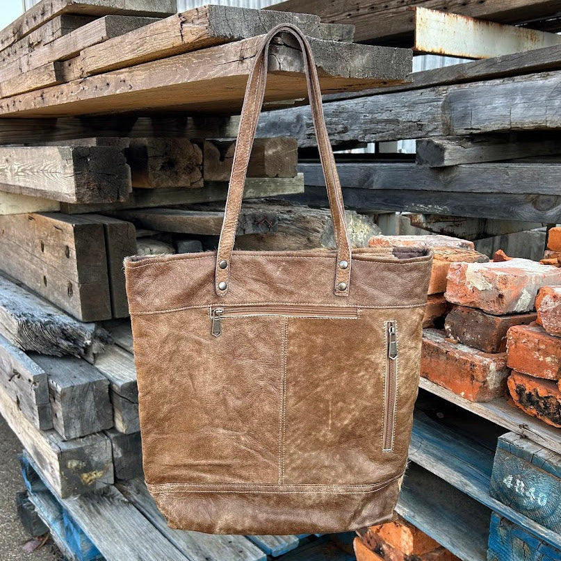 Brown leather tote bag on a background of stacked wooden planks and bricks