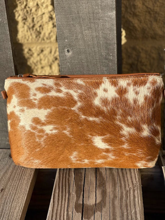 Brown and white cowhide clutch bag on wooden slats