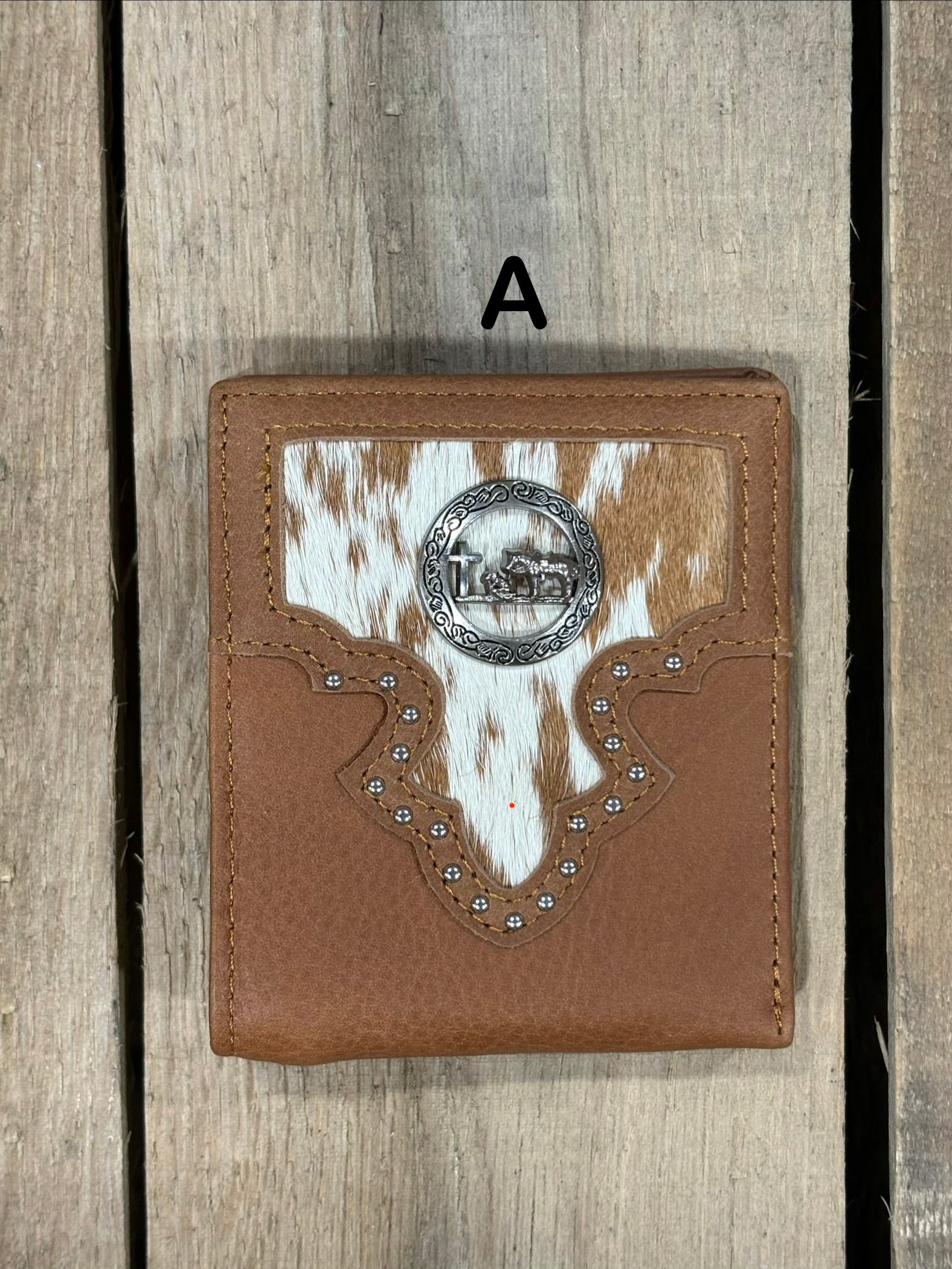 Brown leather wallet with white cowhide pattern and praying cowboy concho on a wooden surface
