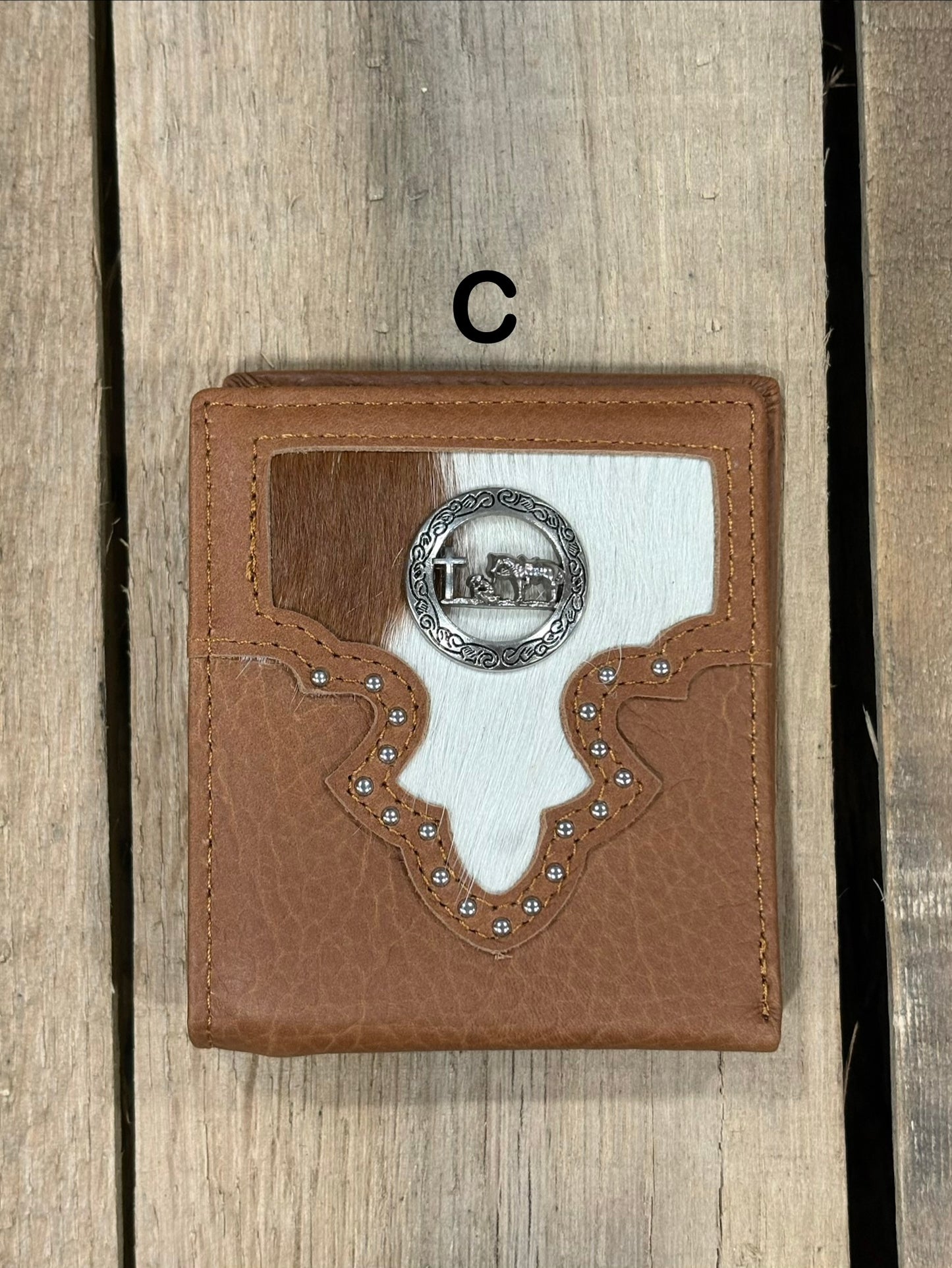 Brown leather wallet with white cowhide pattern and praying cowboy concho on a wooden surface