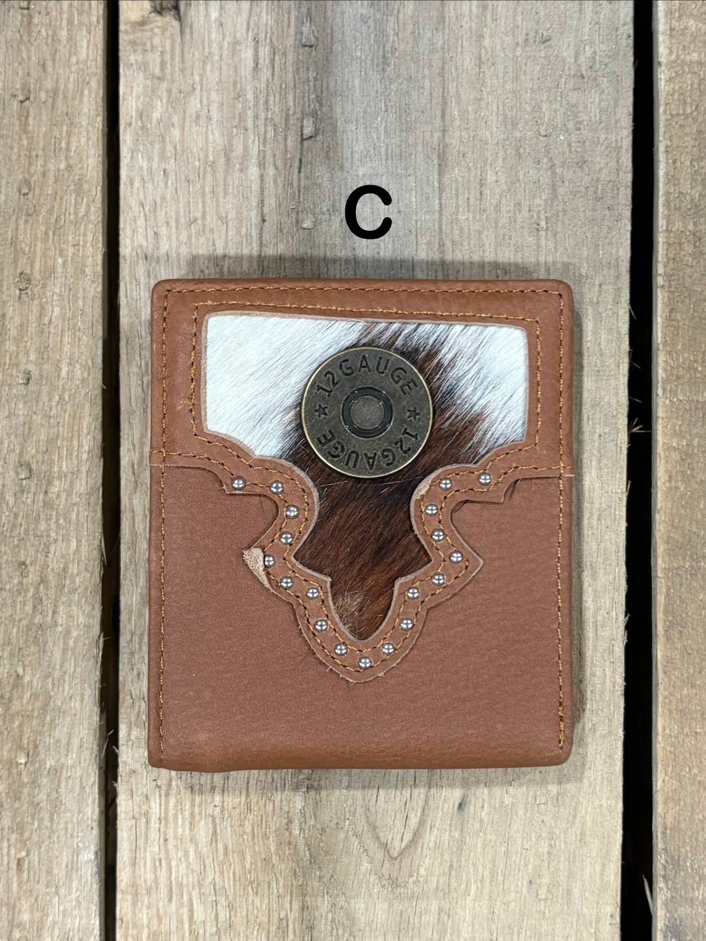 Brown leather wallet with white cowhide pattern and shotgun shell concho on a wooden surface