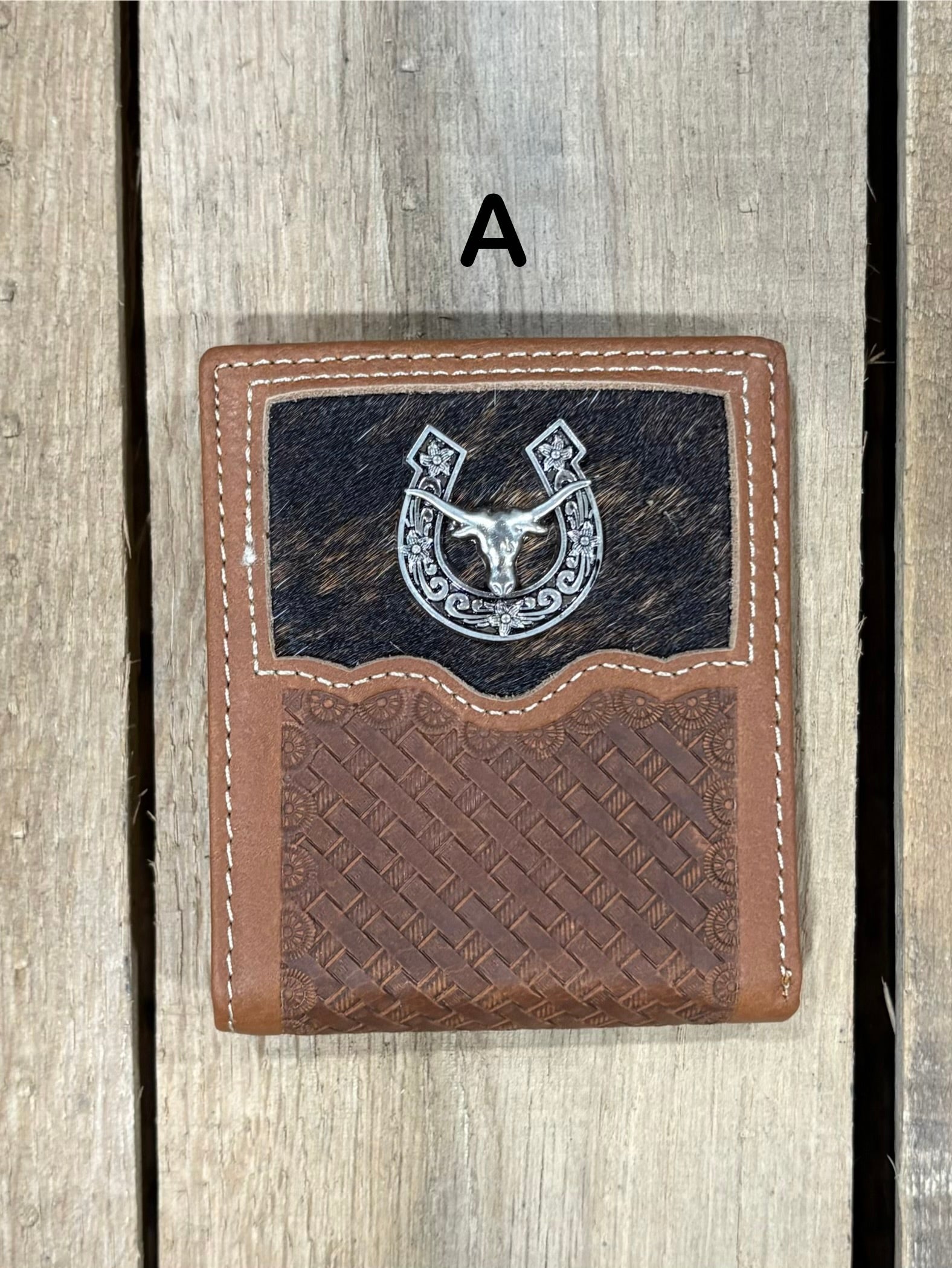 Brown leather wallet with embossed basketweave design and horseshoe and longhorn concho on a wooden surface