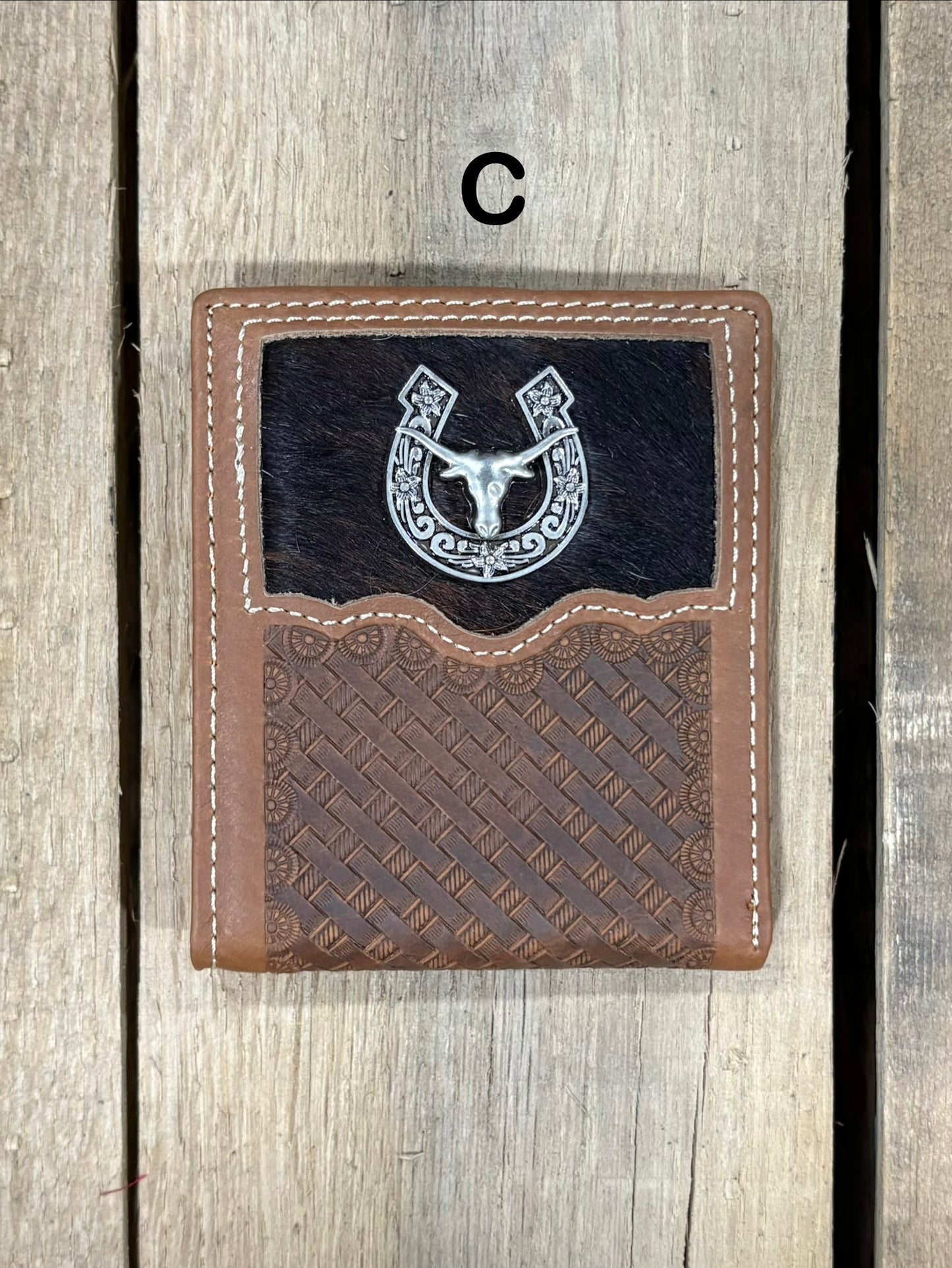 Brown leather wallet with embossed basketweave design and horseshoe and longhorn concho on a wooden surface