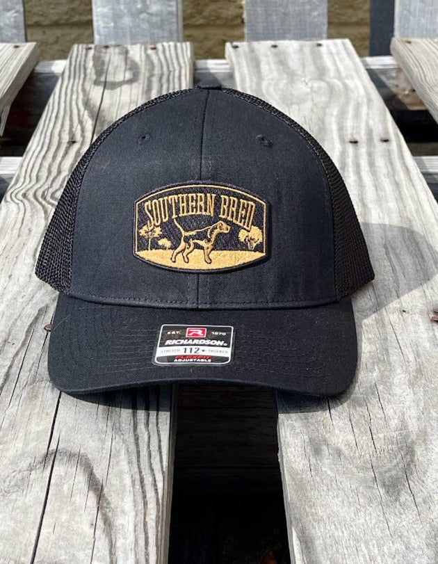 Black cap with a Southern Bred logo on a wooden surface