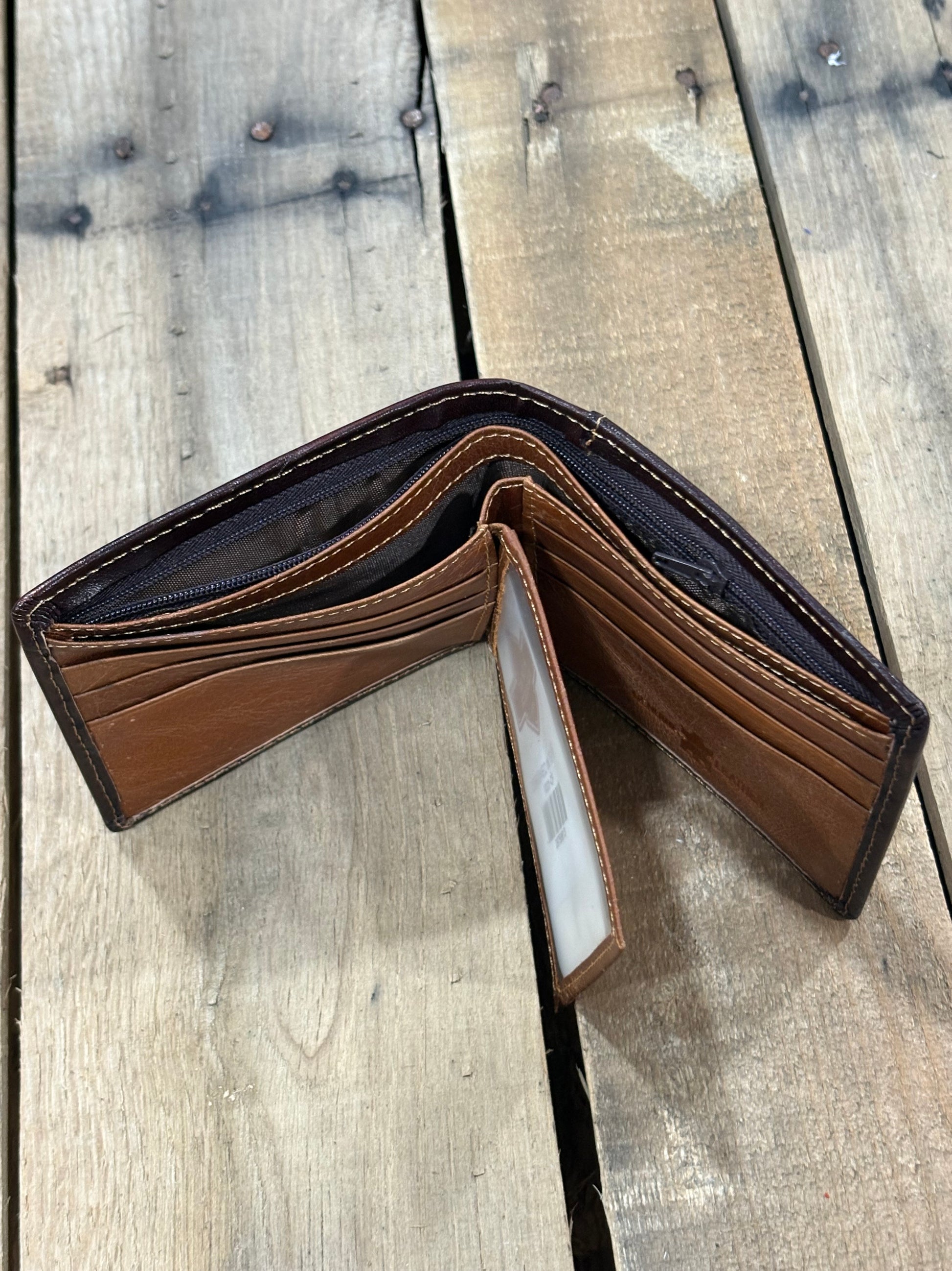 Open brown leather wallet showing card and ID slots and the 2 currency pockets with back zipper compartment on a wooden surface