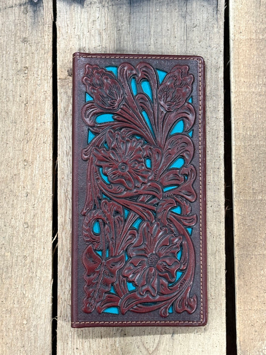 Brown leather wallet with intricate floral patterns on a striped fabric surface with a wooden wheel in the background.