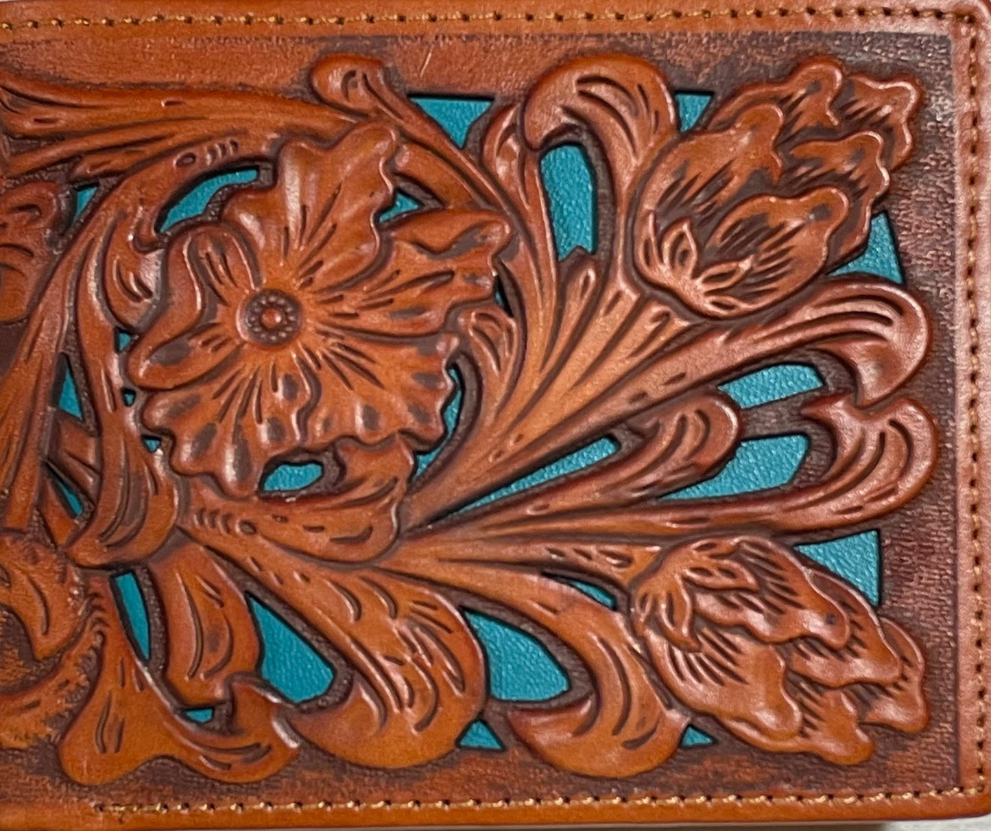 Close-up of a brown leather wallet with intricate floral tooled design on a turquoise background