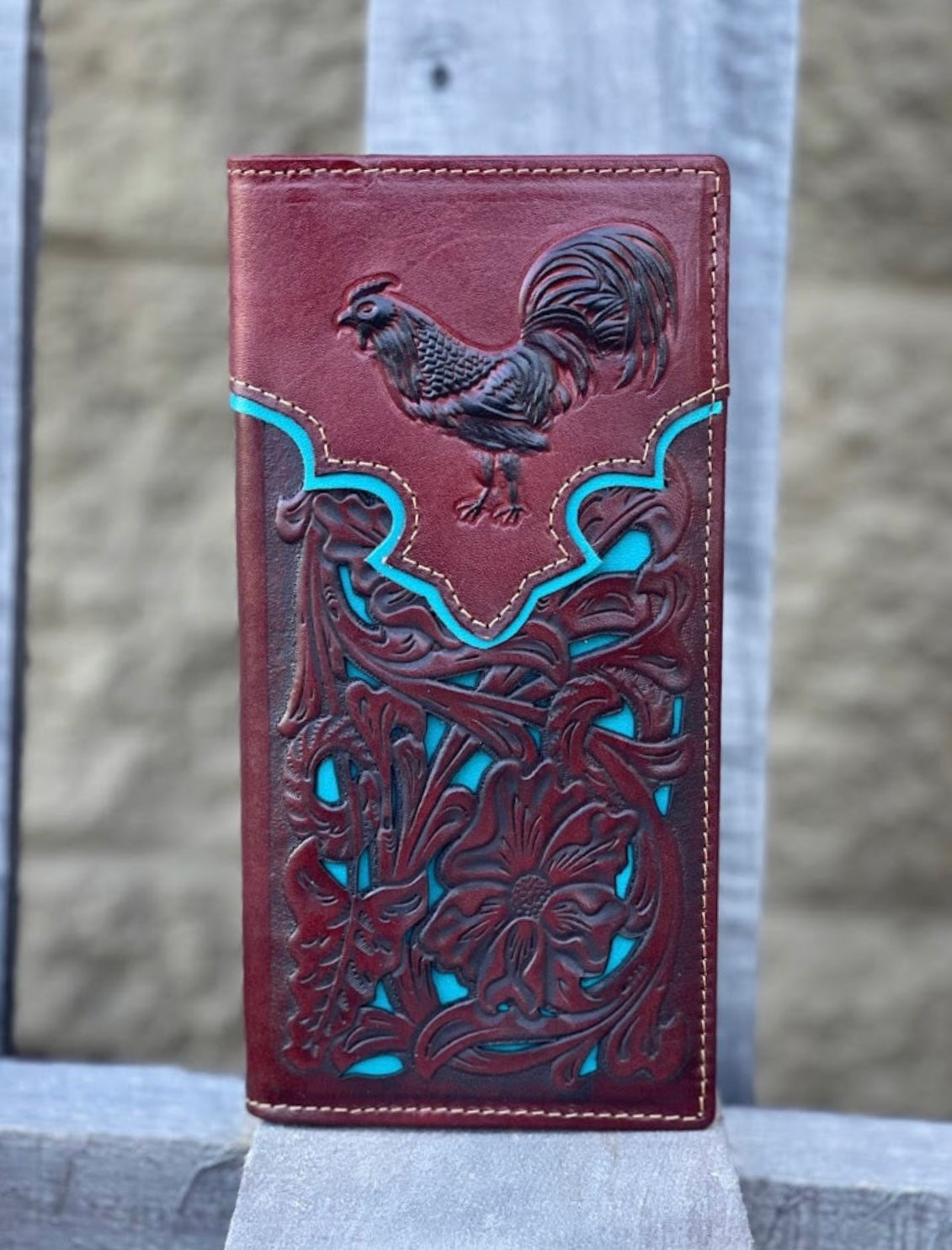 Brown leather wallet with rooster design on a stone surface