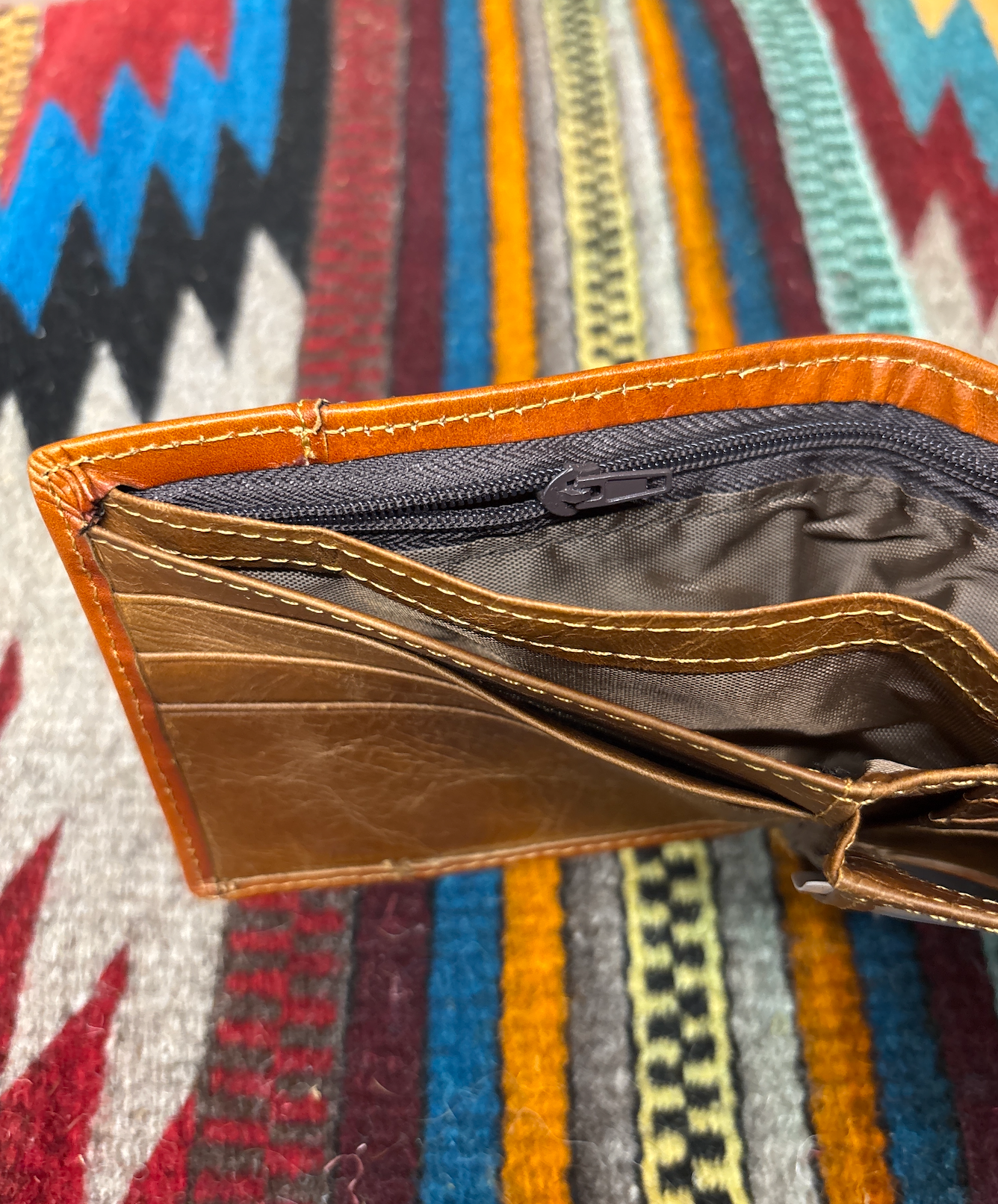 Brown leather wallet open against a view of the inside zipper pocket with fabric background.