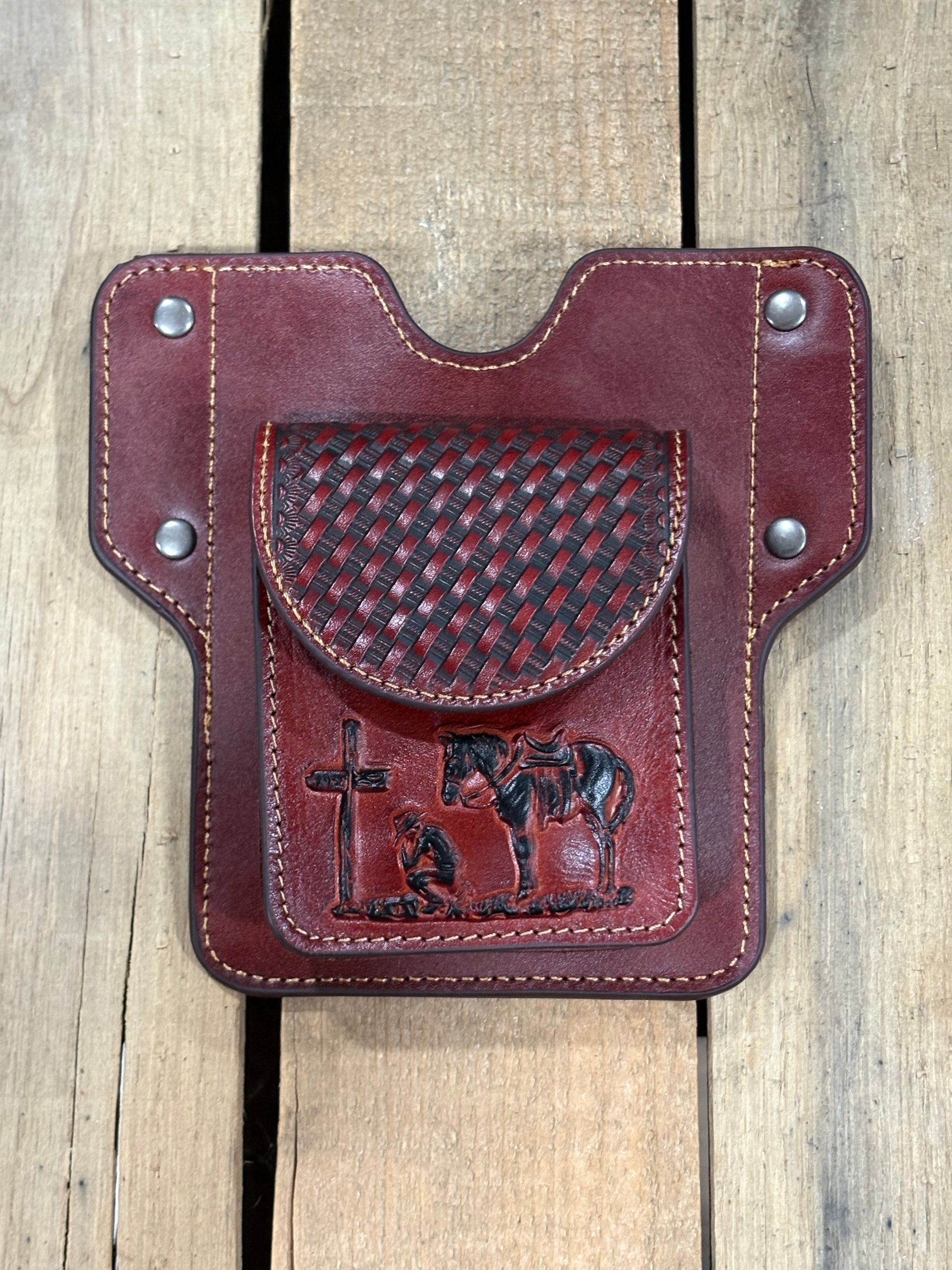 Brown leather pouch with basketweave and embossed praying cowboy design on a wooden surface