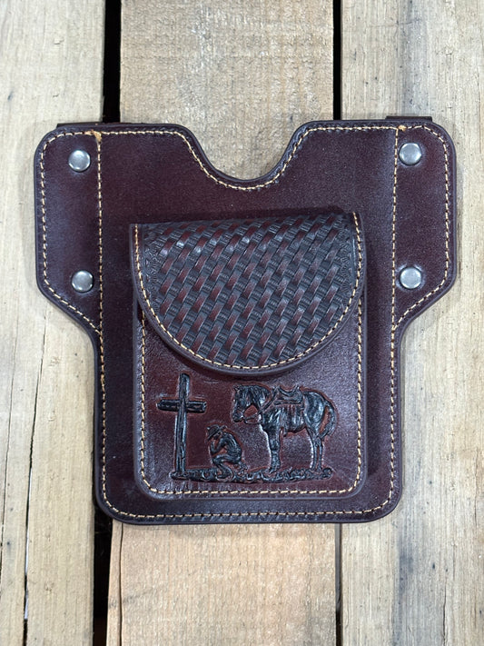 Front view of a coffee brown leather phonecase with basketweave and embossed praying cowboy design on a wooden surface