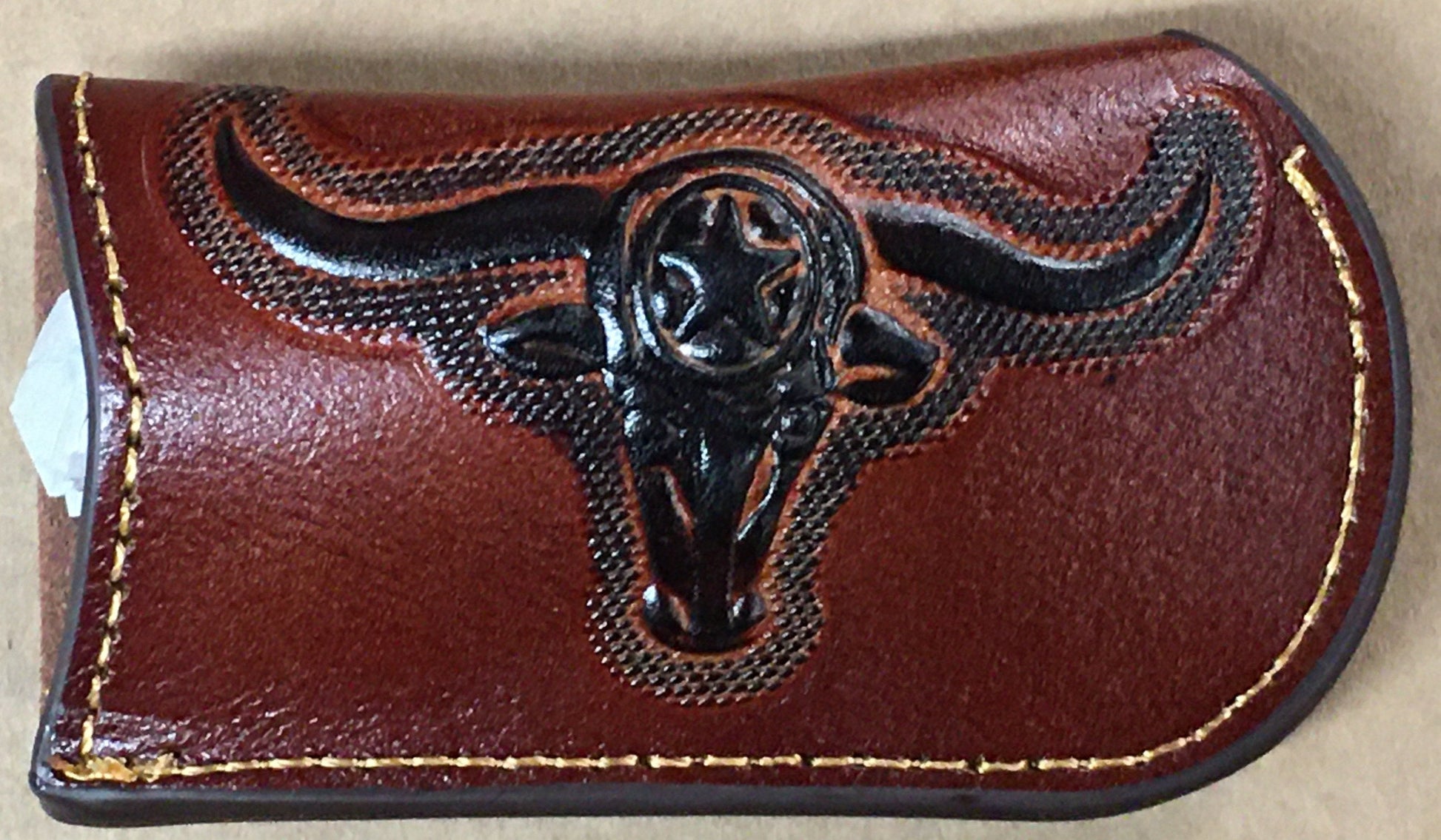 Brown leather cardholder with black bull skull design on a beige background