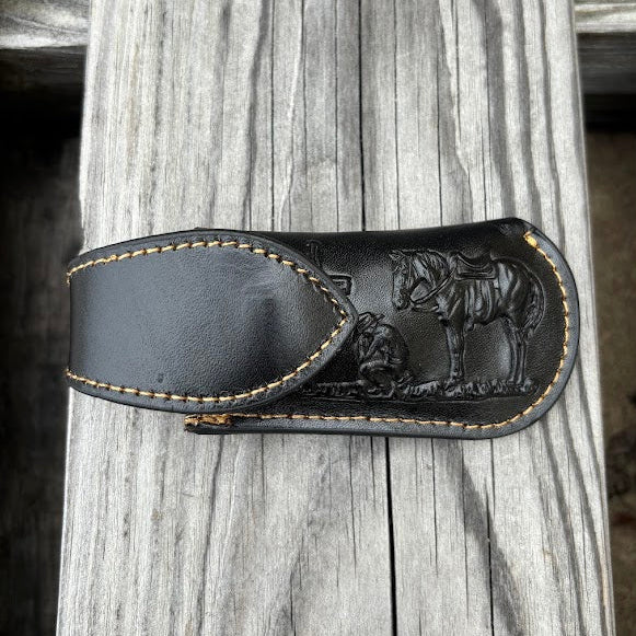 Black leather knife sheath with embossed design on a wooden surface