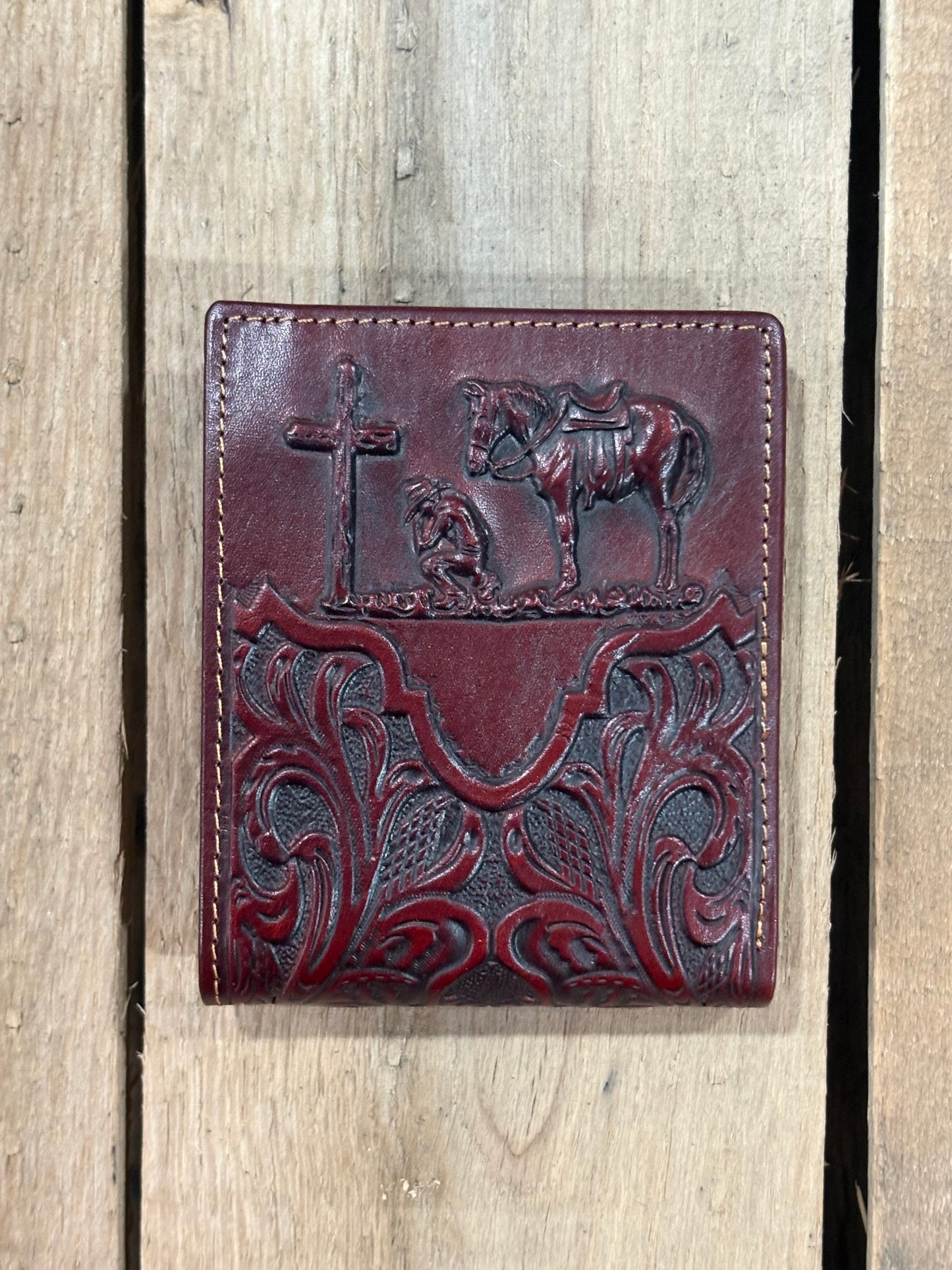 Close up of a Dark Brown leather wallet with embossed designs of a cross, horse, and cowboy on a wooden background