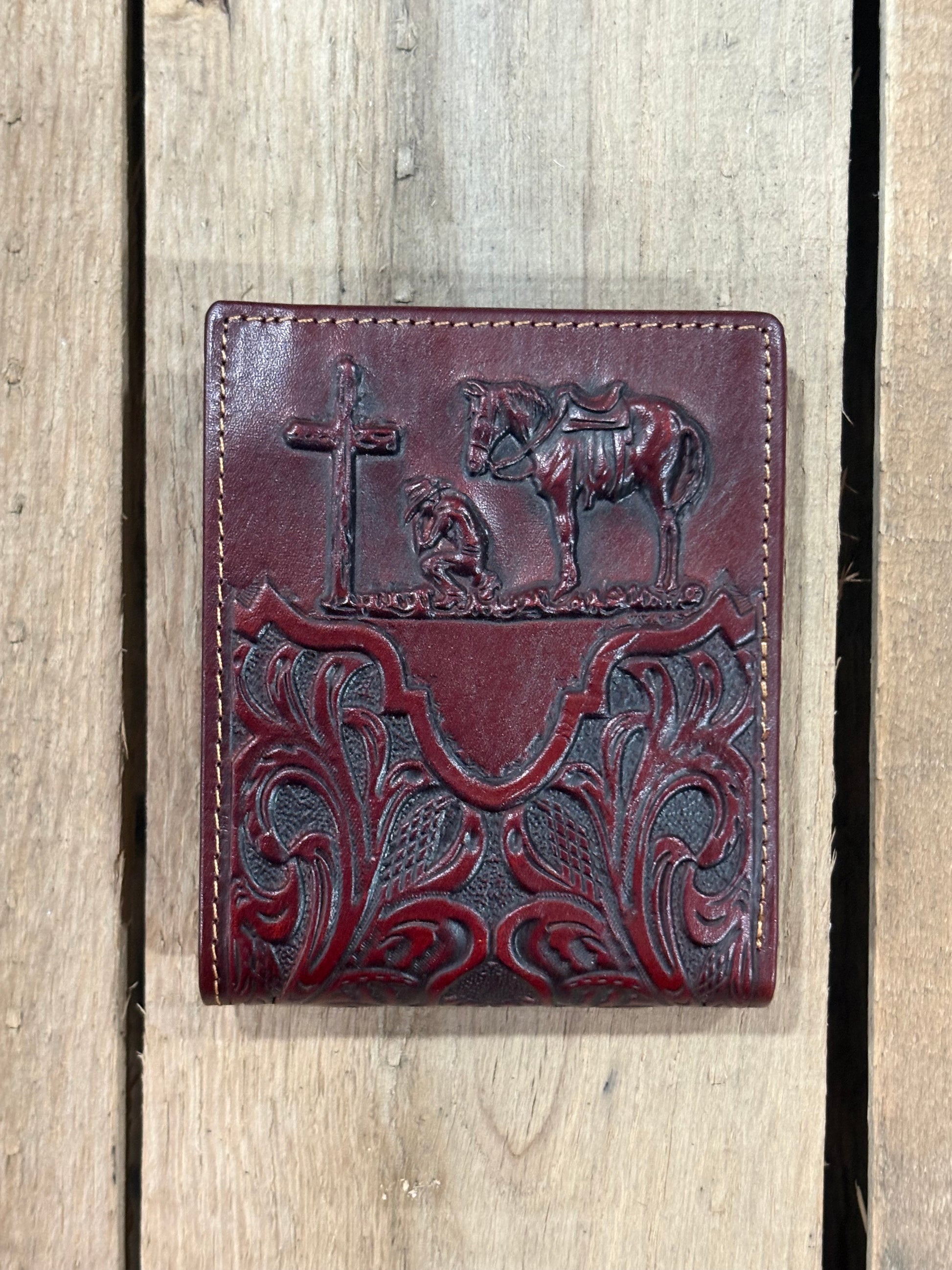 Close up of a Dark Brown leather wallet with embossed designs of a cross, horse, and cowboy on a wooden background