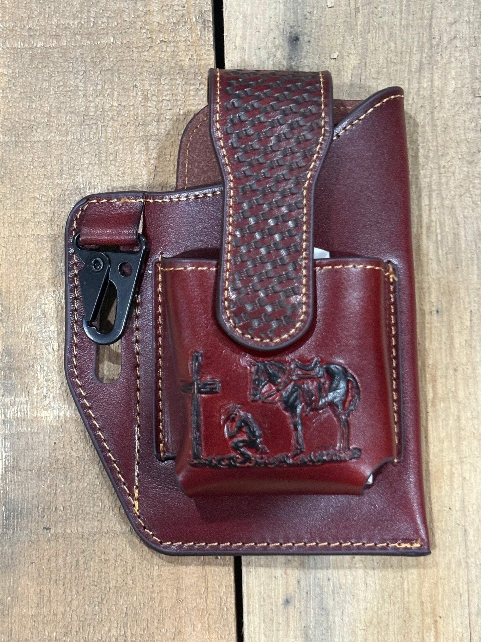 Brown leather holster with pouch and praying cowboy embossed design on a wooden surface