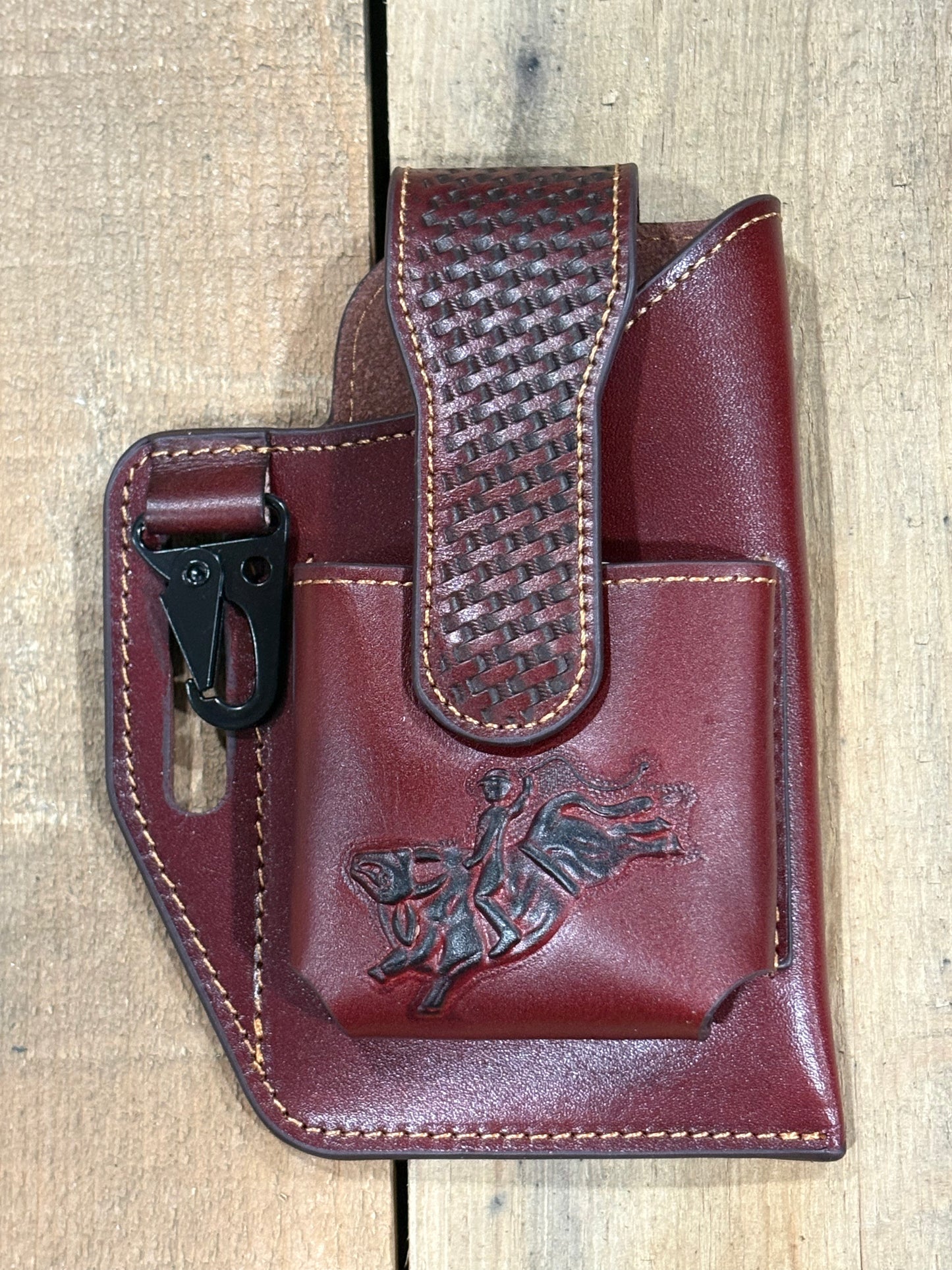 Brown leather holster with pouch and a bull rider embossed design on a wooden surface
