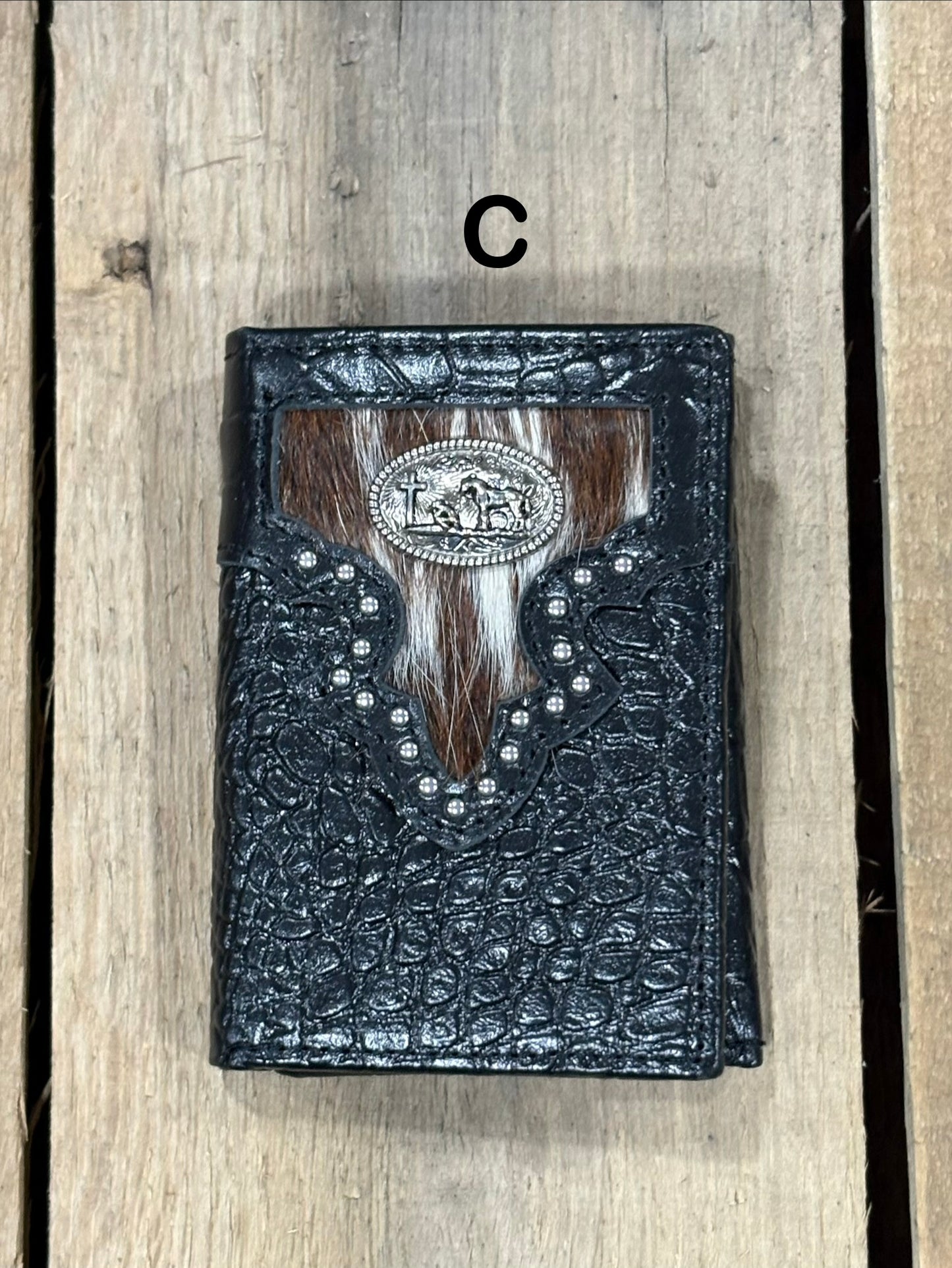 Black leather alligator print wallet with brown and white hairon cowhide, praying cowboy concho on a wooden surface