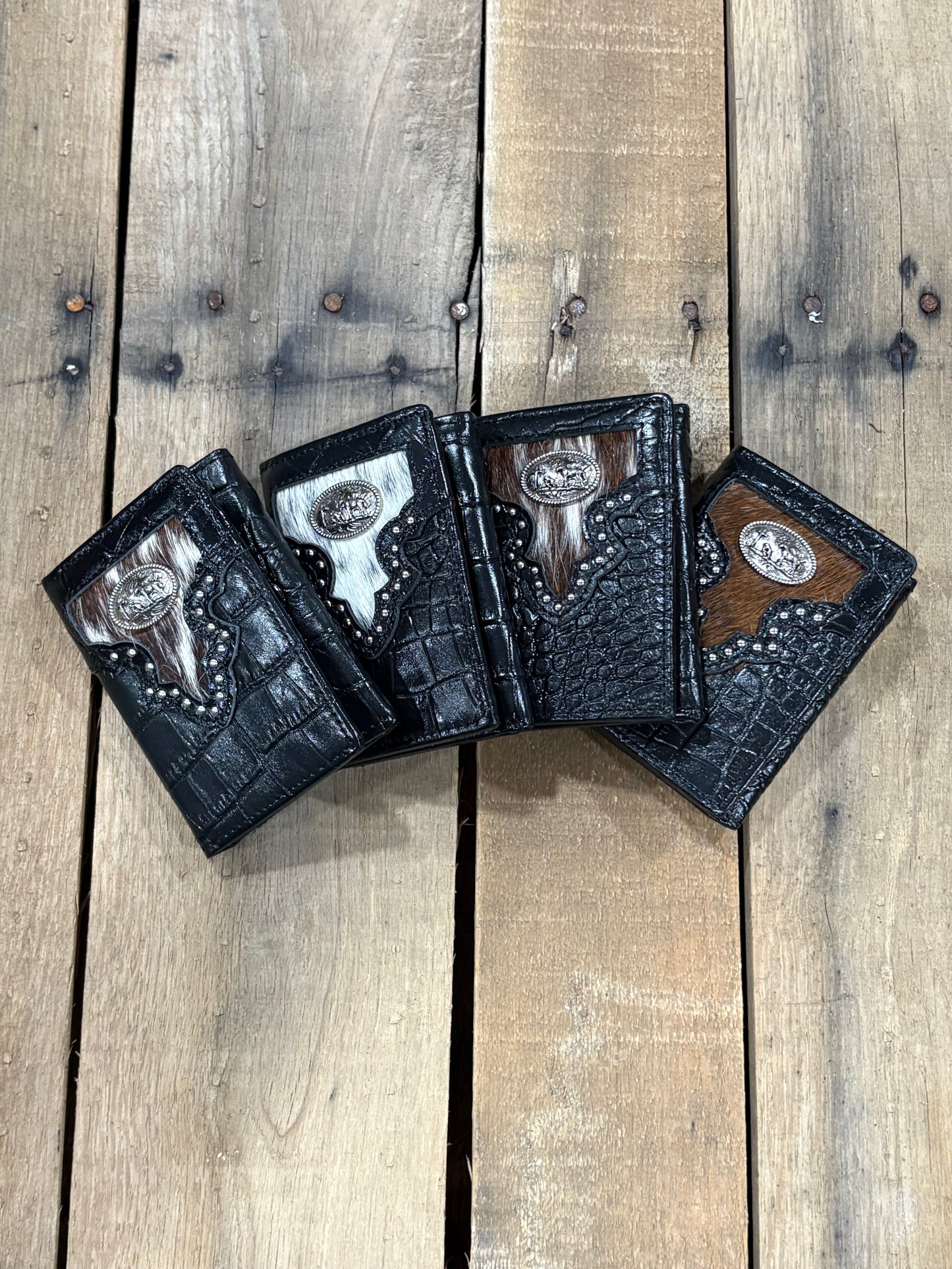 Four black leather wallets with studded details on a wooden surface