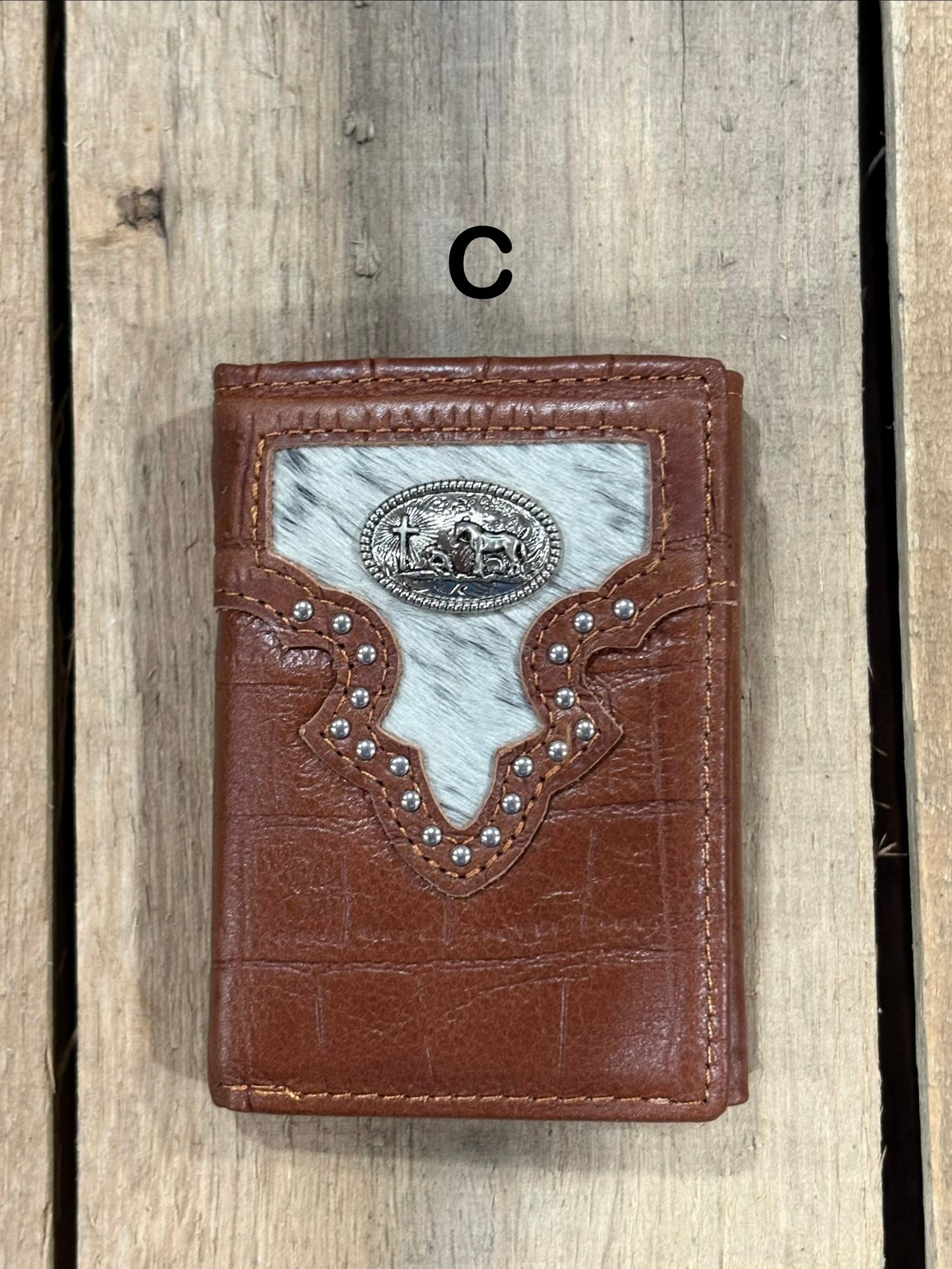 Brown leather alligator print wallet with black and white hairon cowhide, praying cowboy concho on a wooden surface