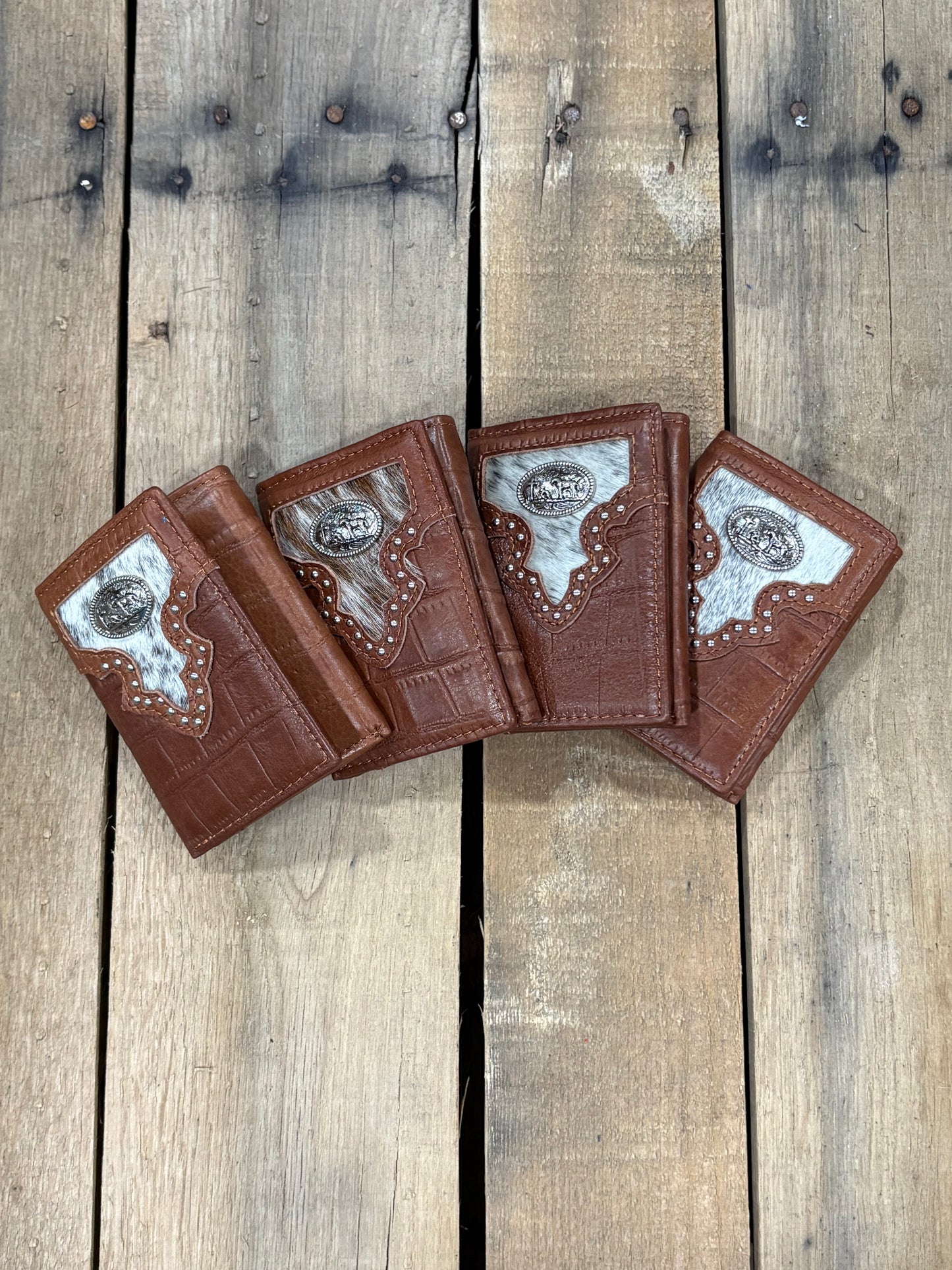 Four brown leather wallets with decorative elements on a wooden surface