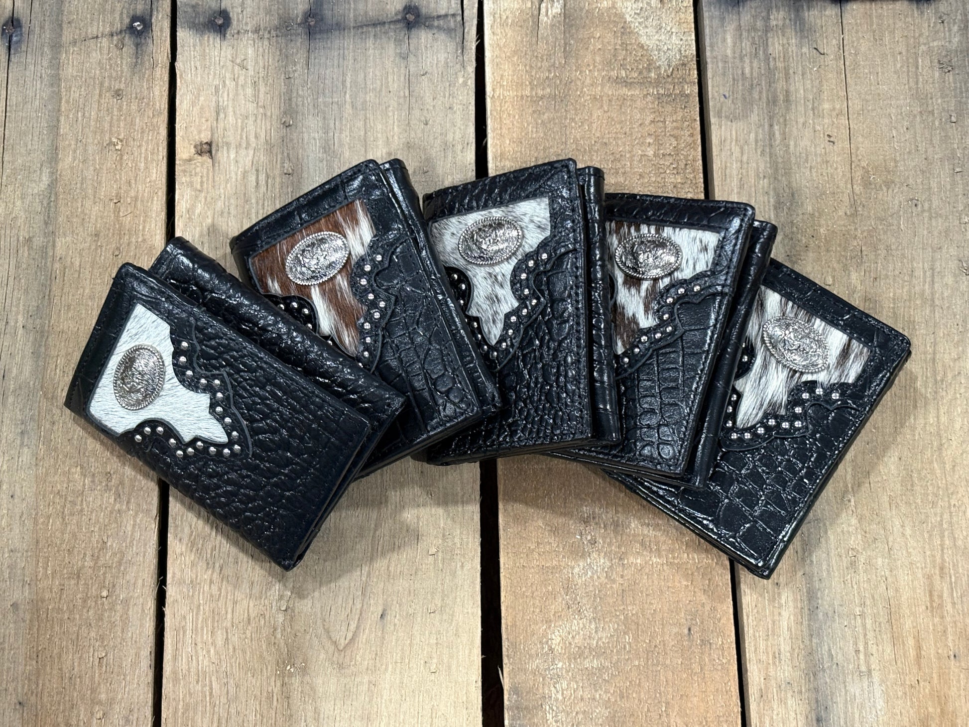 Five black leather wallets with silver Rooster conchos on a wooden surface