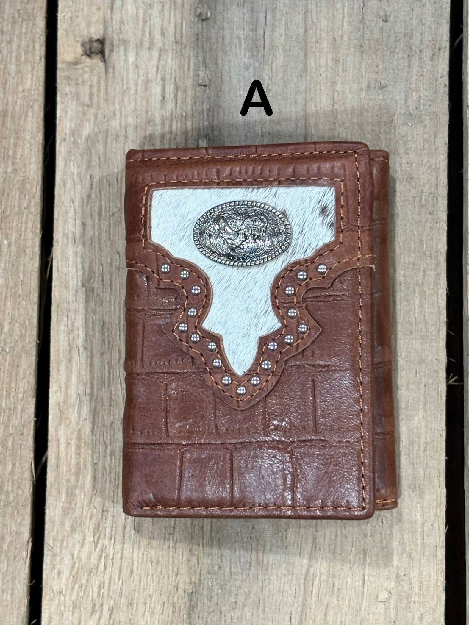 Brown leather alligator print wallet with hairon cowhide and silver rooster concho on a wooden surface