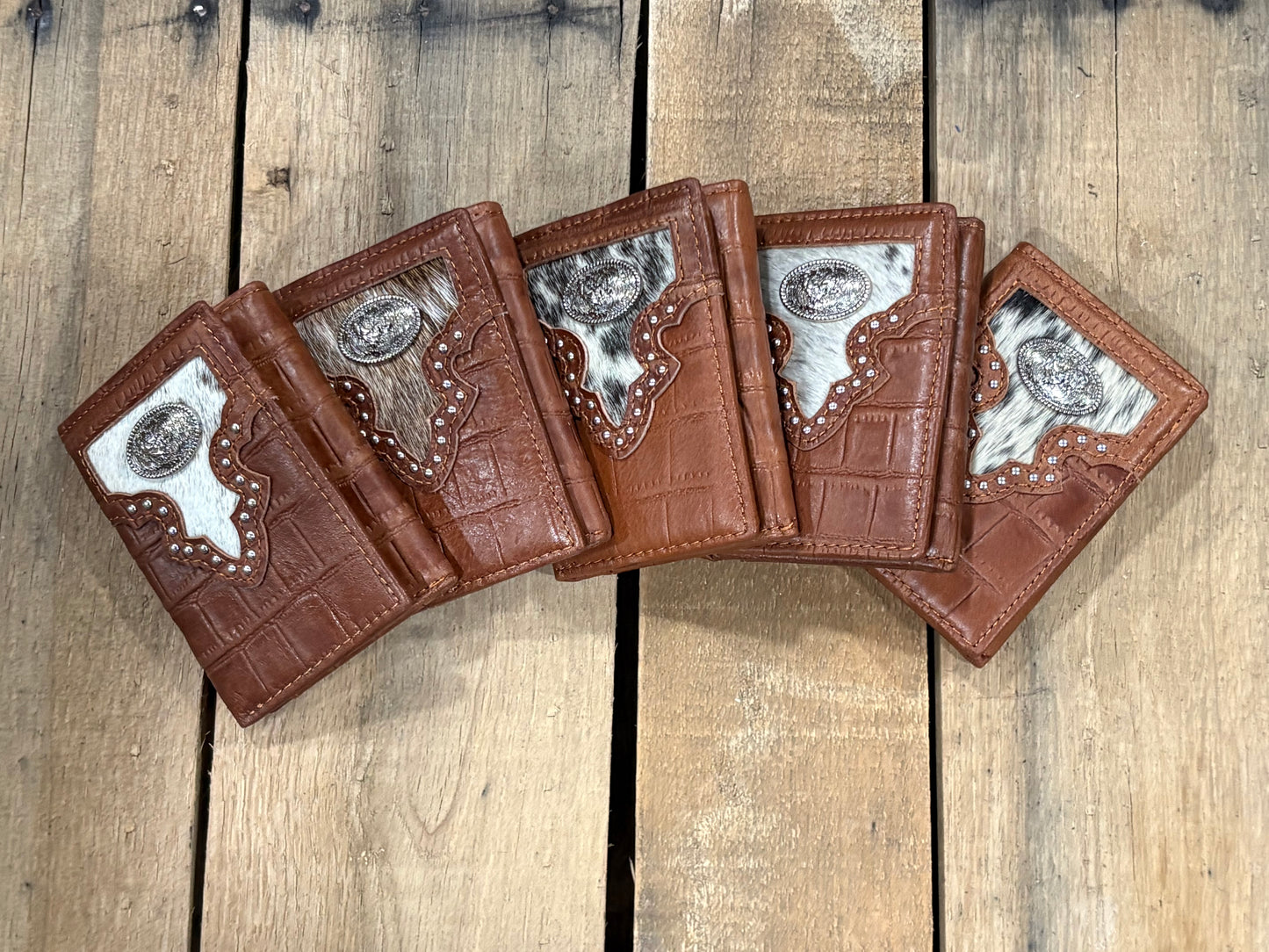 Five brown leather wallets with silver rooster concho designs on a wooden surface