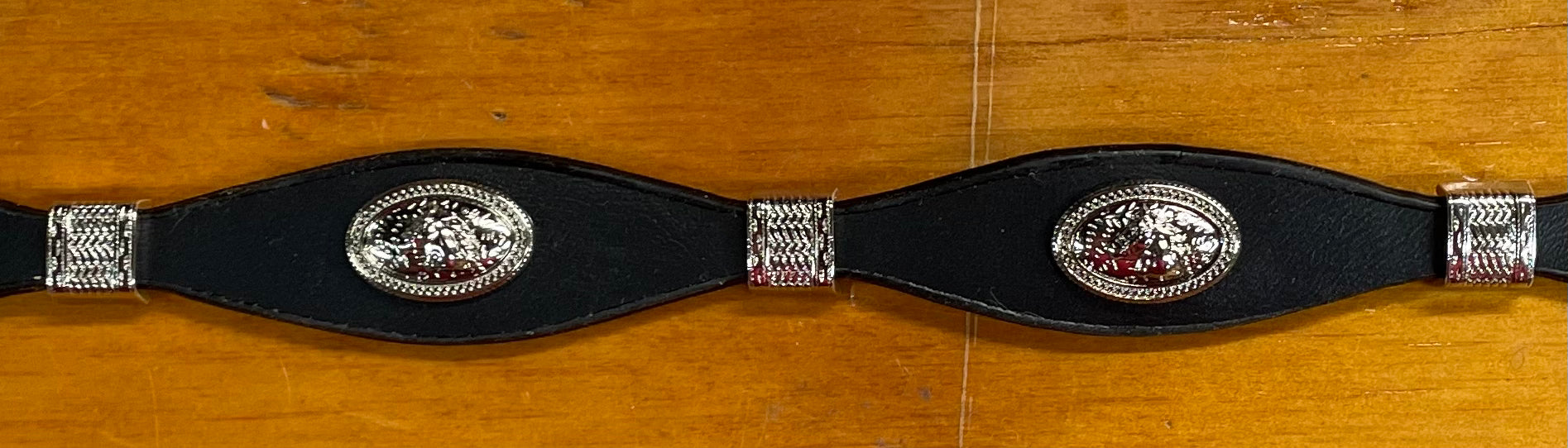 Black leather hat band with a Horse Head Concho with silver bands separating them. This hat band is fully adjustable with a Western style buckle. On wooden background.