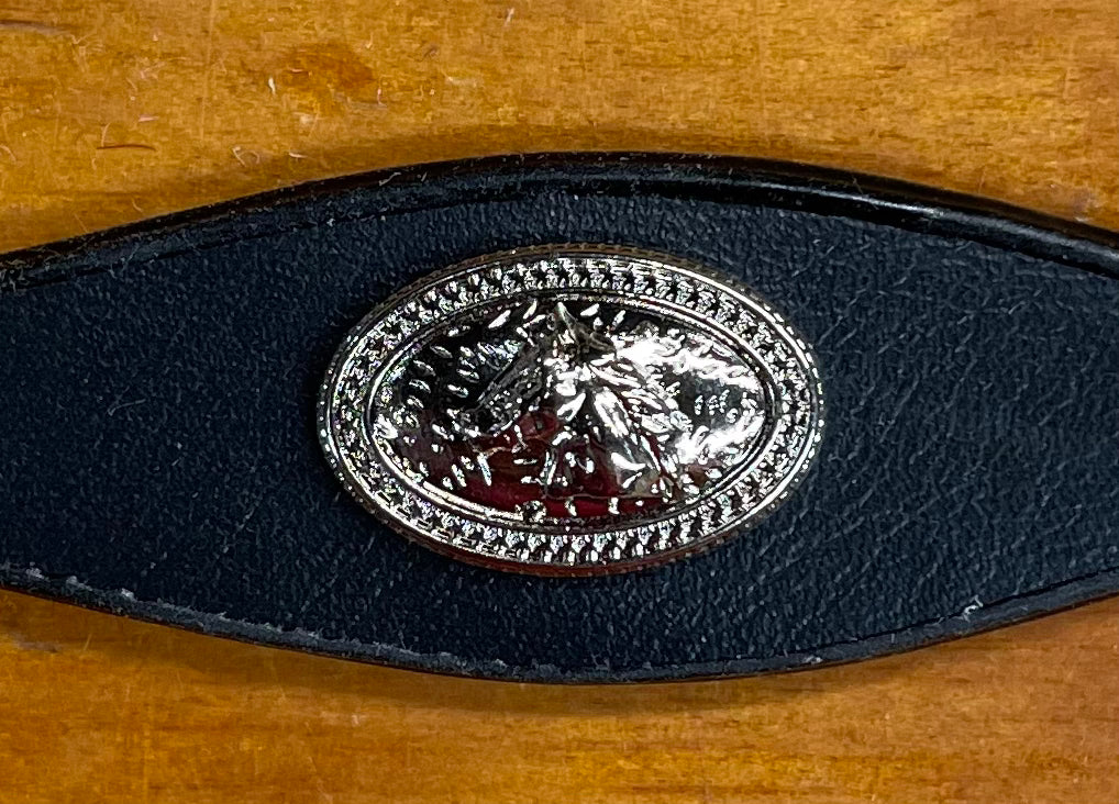 Silver Concho with Horse head figure on it. Black leather band on wooden background.