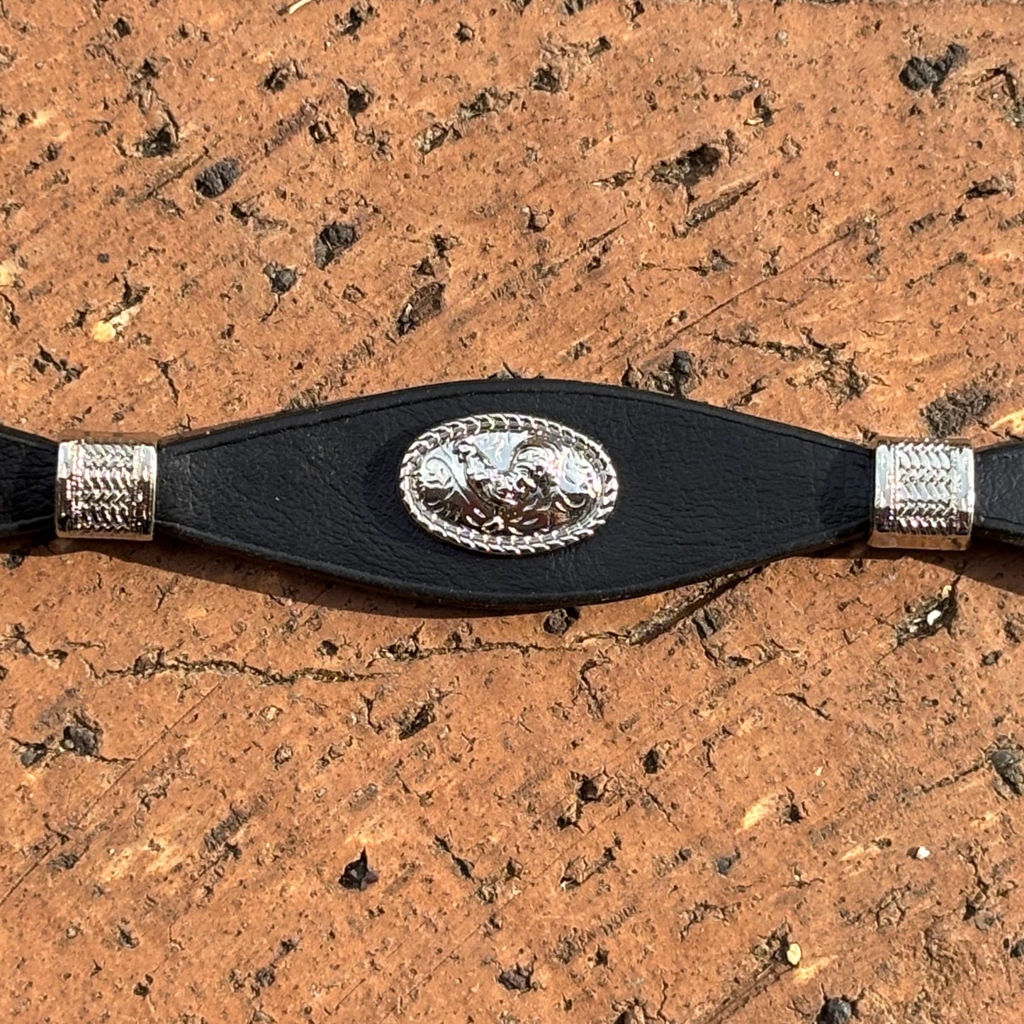 Decorative black leather hat band and silver buckle set and conchos on a wooden background