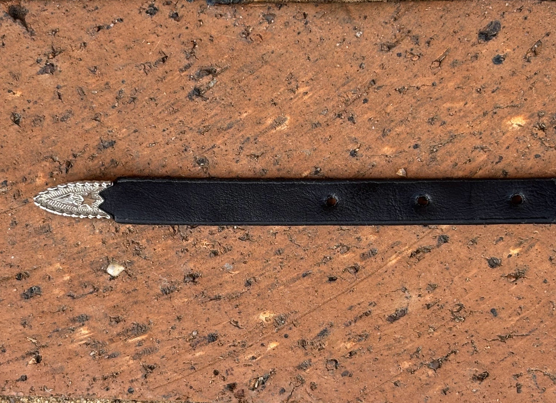 Black leather hat band with silver tip on a wooden surface