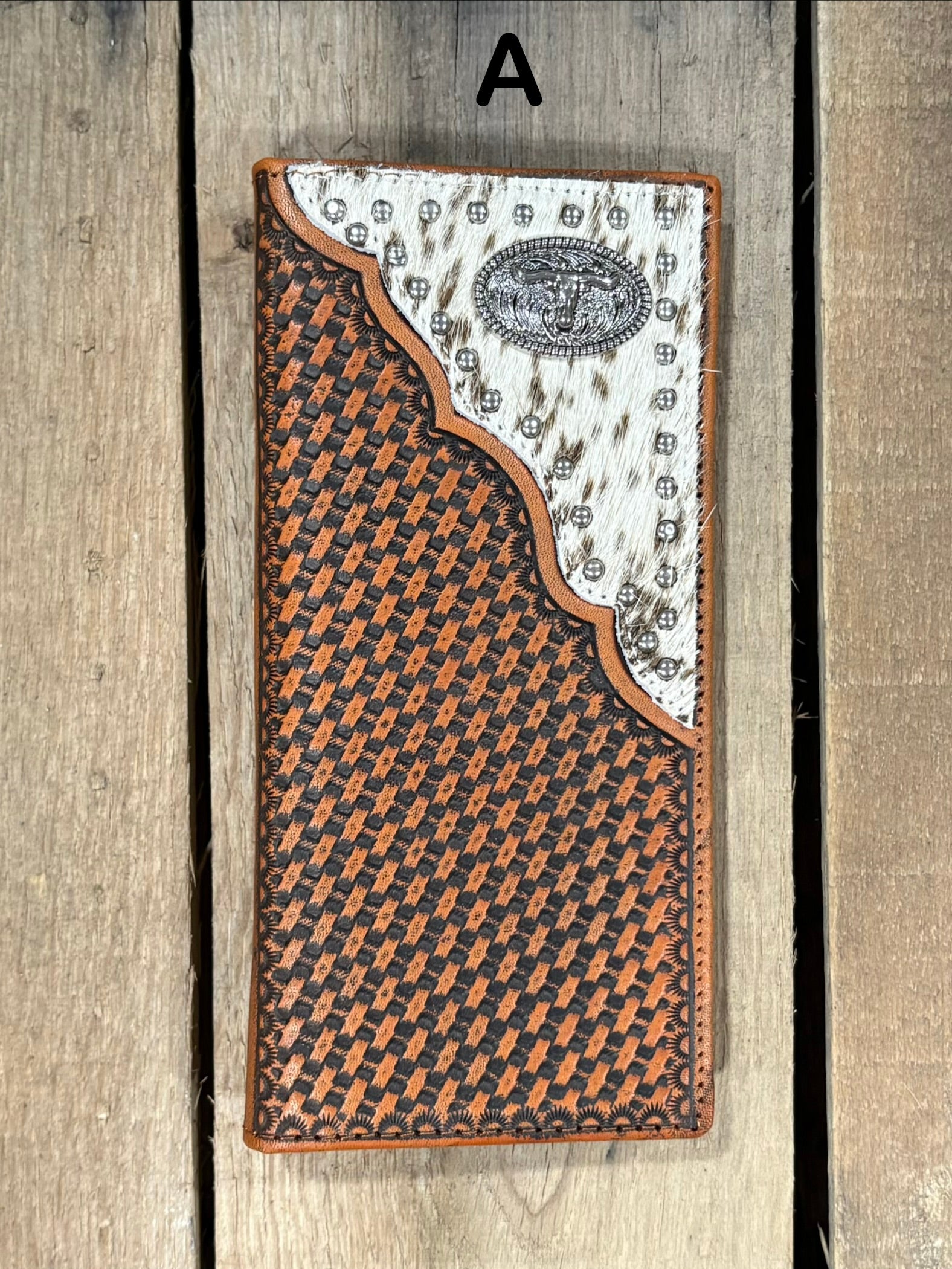 Leather wallet with basketweave pattern and white hair-on corner with Longhorn concho on a wooden surface