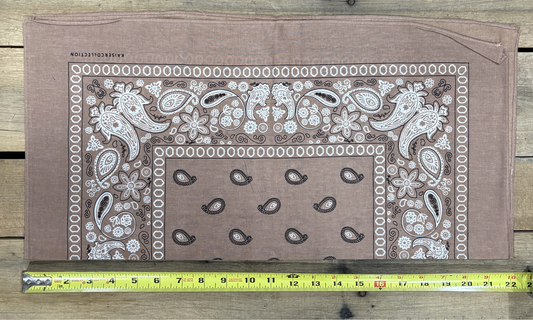 Natural Brown bandana with white paisley patterns on a wooden surface, measured by a yellow tape measure.