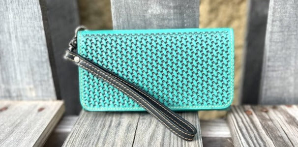 Turquoise woven clutch with a black strap on a wooden surface