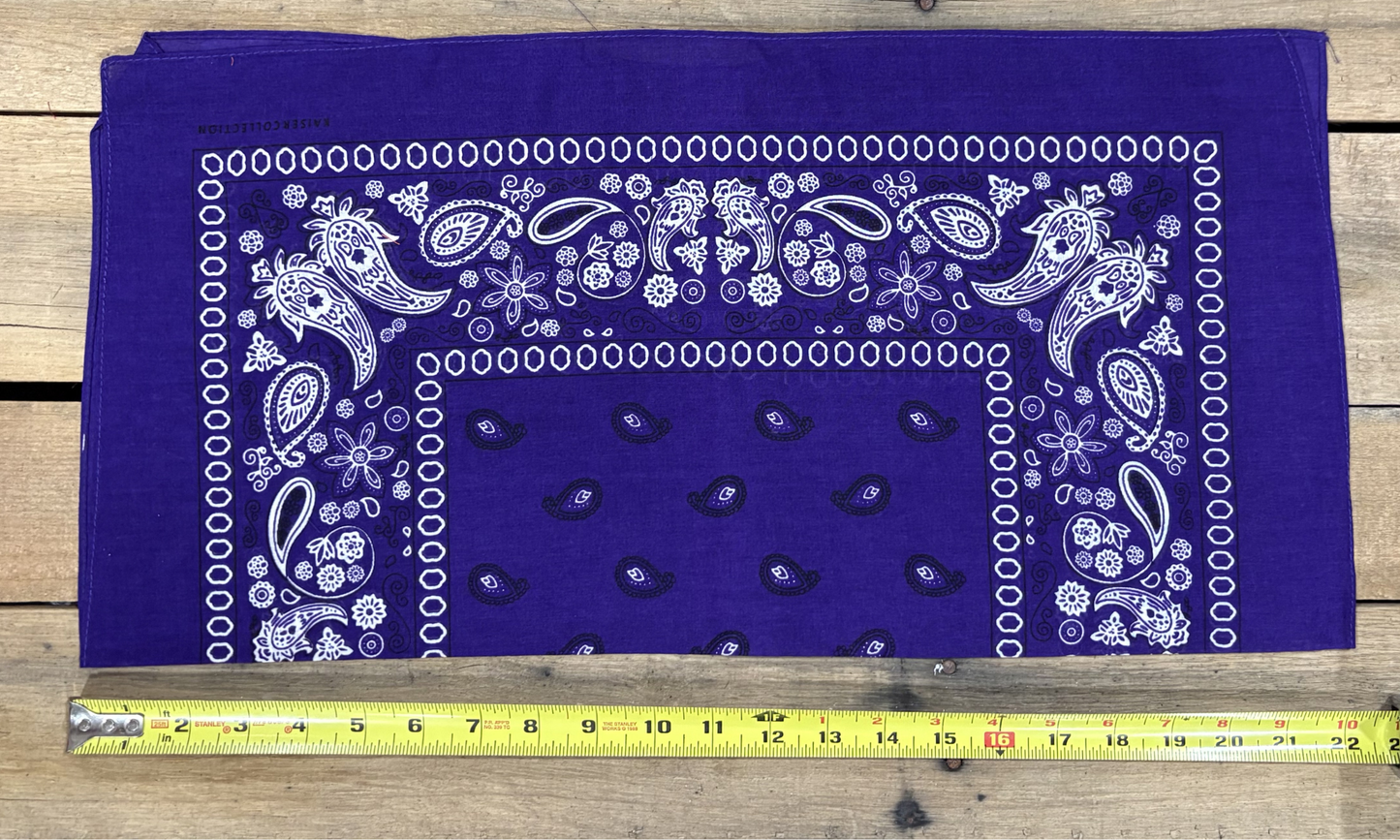 Purple bandana with white paisley patterns on a wooden surface, measured by a yellow tape measure.